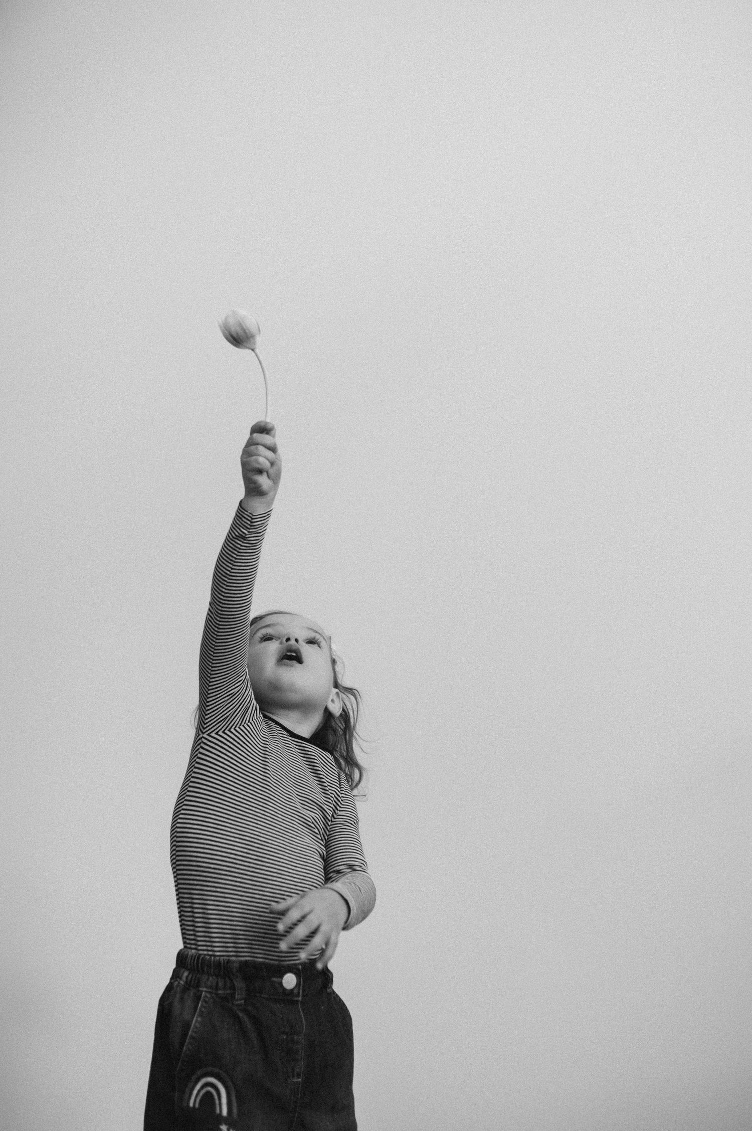 Black and white photos of a young child reaching upward in a striped shirt.