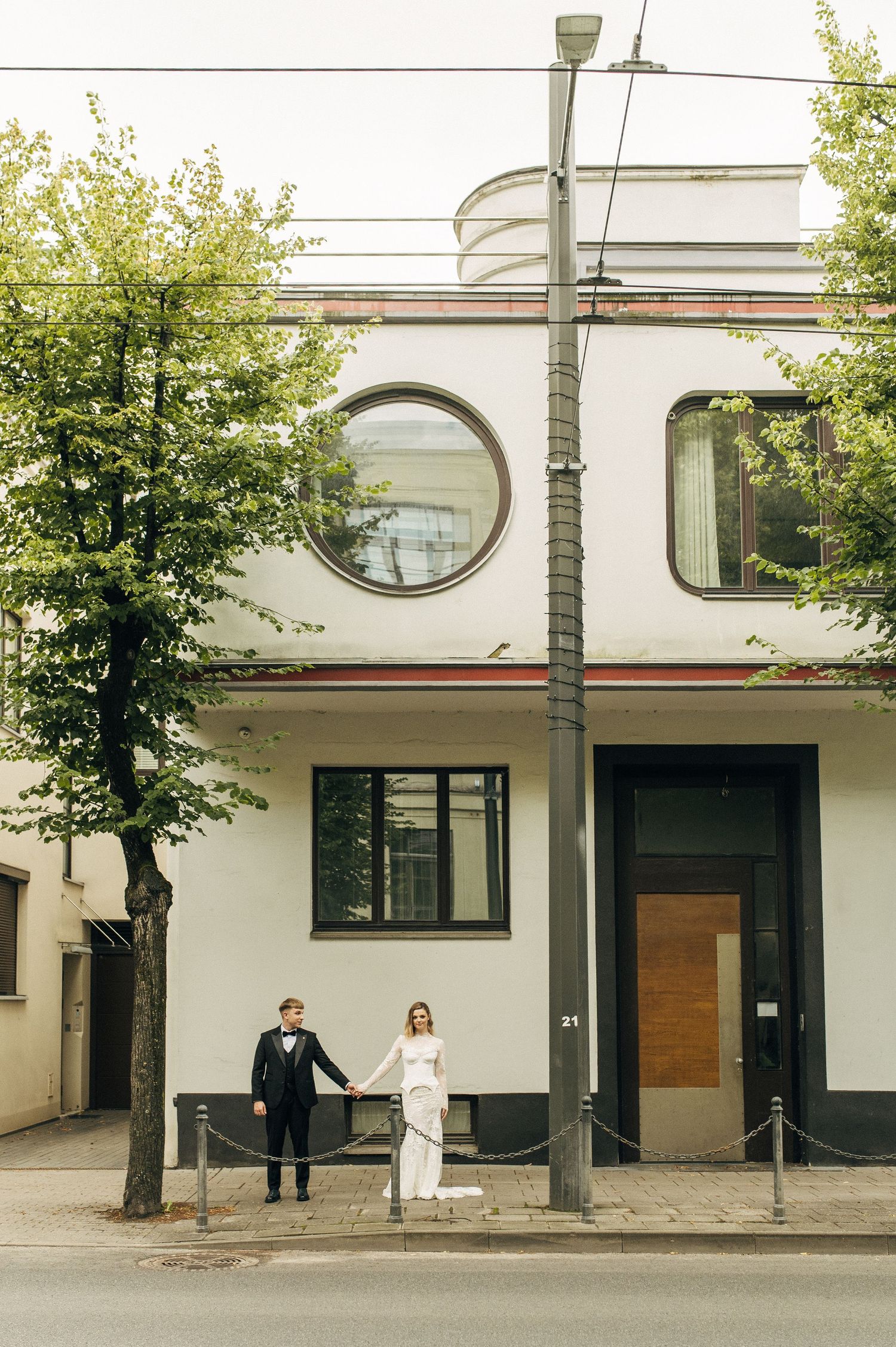 Modern minimalist building exterior with white walls, oval windows and trees lining the street in an urban setting.