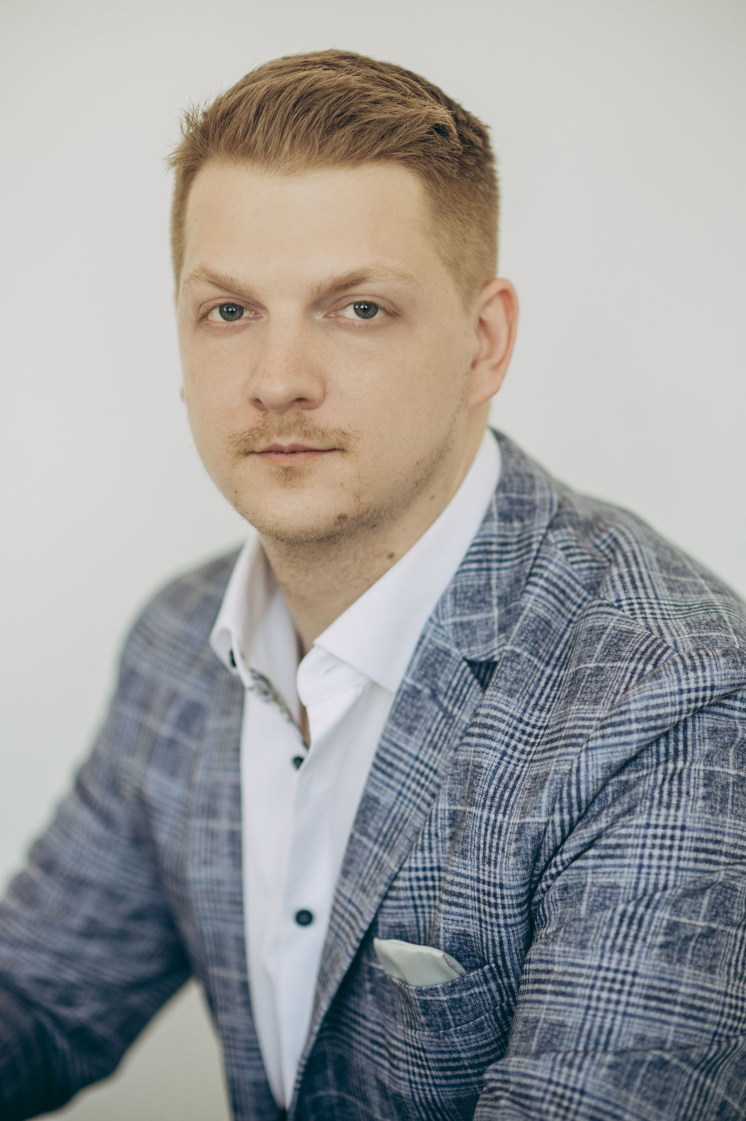 Business portrait of someone wearing a plaid grey suit jacket with white shirt against light backdrop.