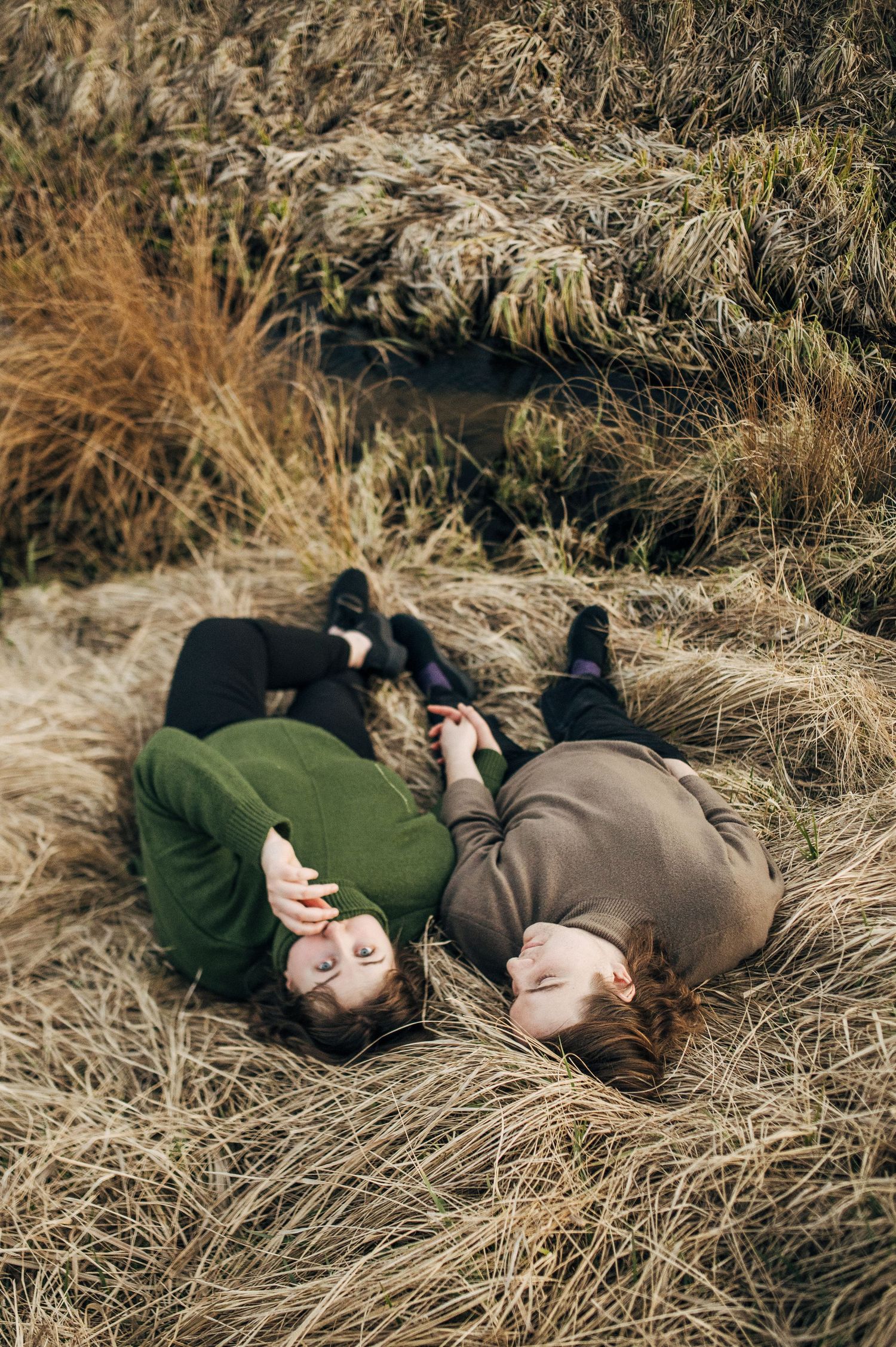 Two people lying in dried grass field during golden hour photography session.