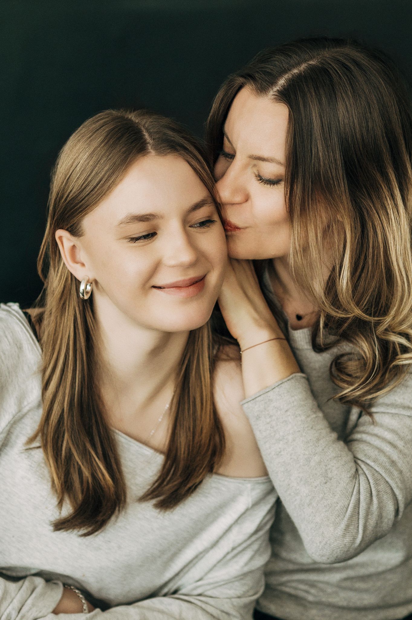 Intimate close-up portrait showing gentle affection between two people in grey sweaters.