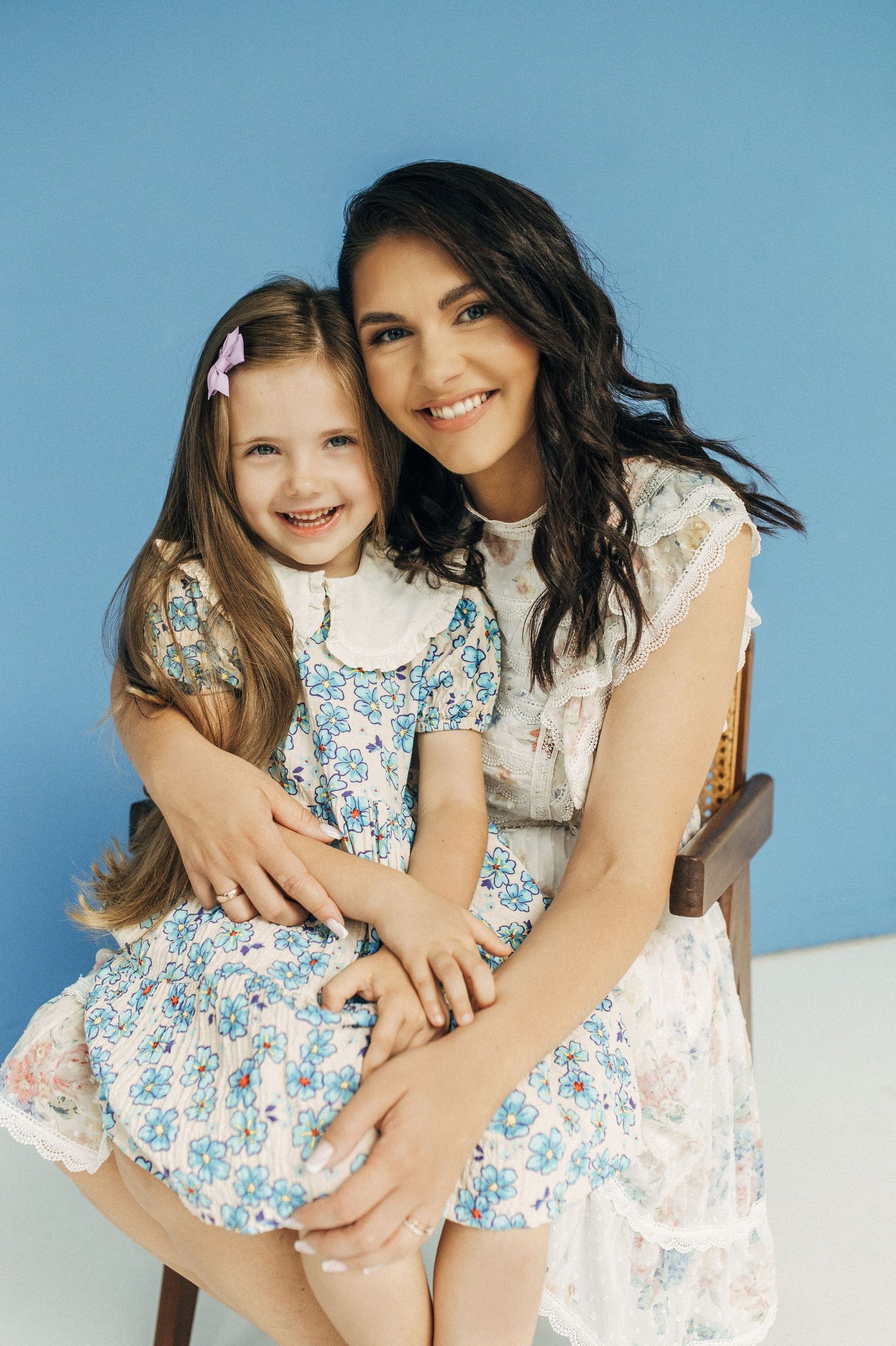 Studio portraits against blue backdrop showcasing joyful embraces in floral dresses.