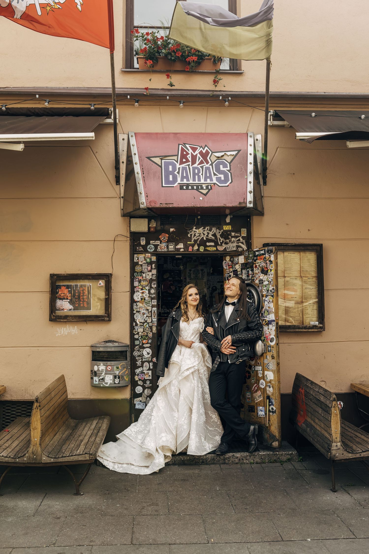 Bride and groom posing outside Baras bar entrance decorated with pins and badges on their wedding day.