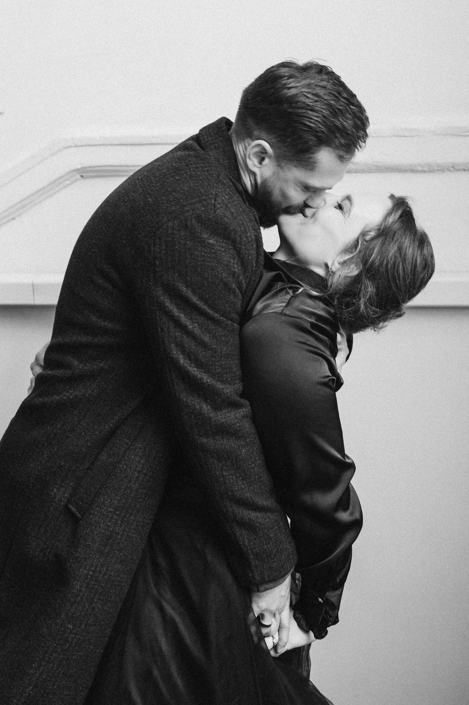 A dramatic black and white portrait of a couple in formal wear sharing a passionate embrace.
