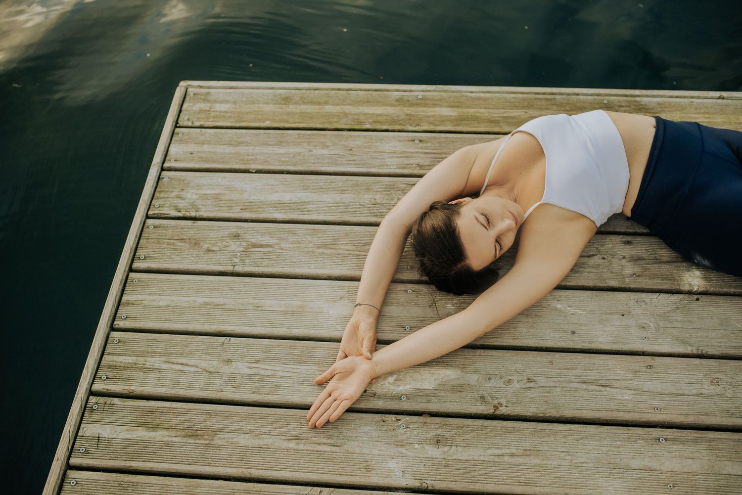 Figure lies peacefully on wooden dock during sunset by the water.