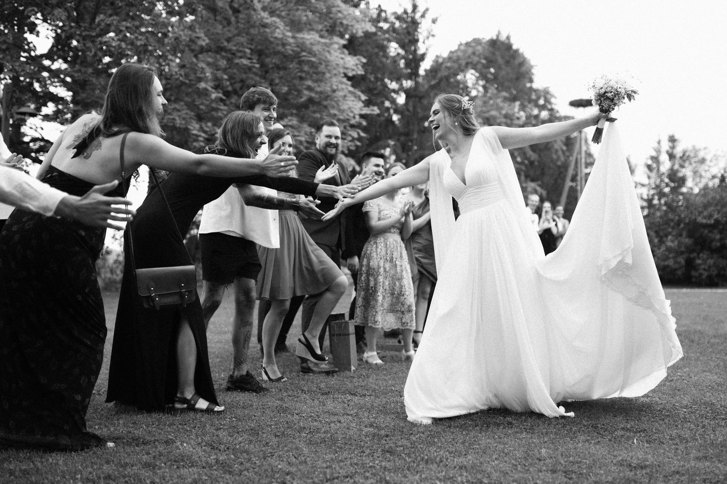 Wedding guests toss flower petals during an outdoor celebration on a sunny day.