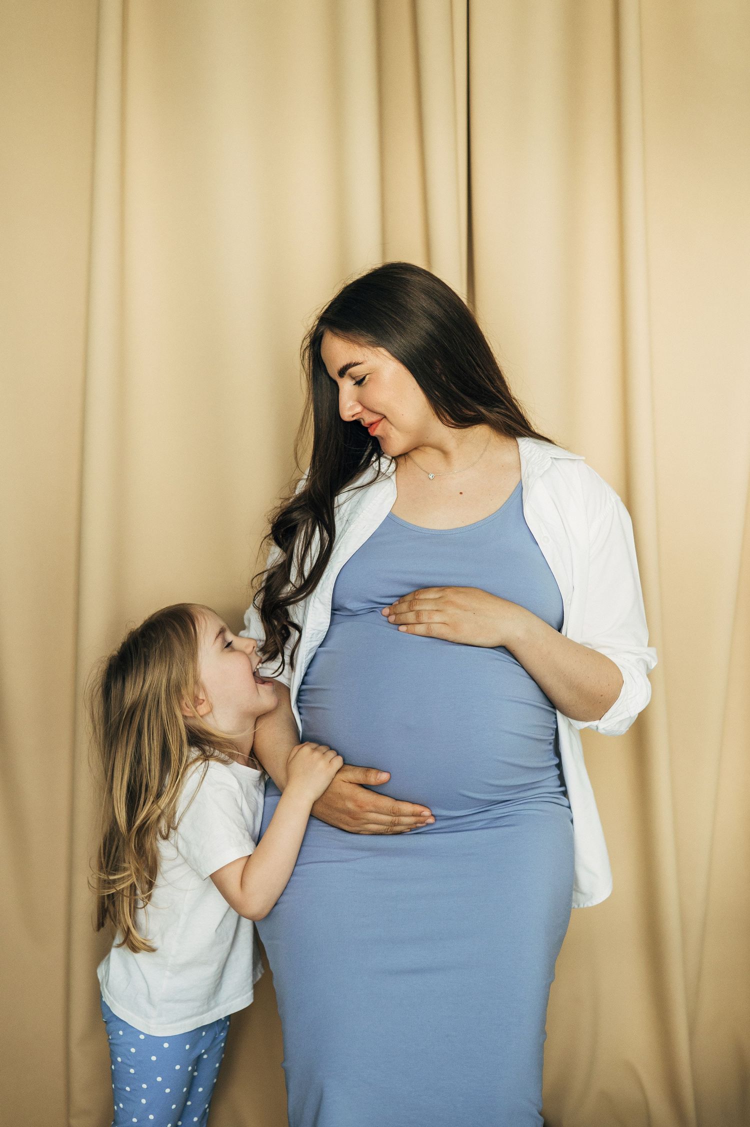 Two figures share tender moments against a beige curtain backdrop.