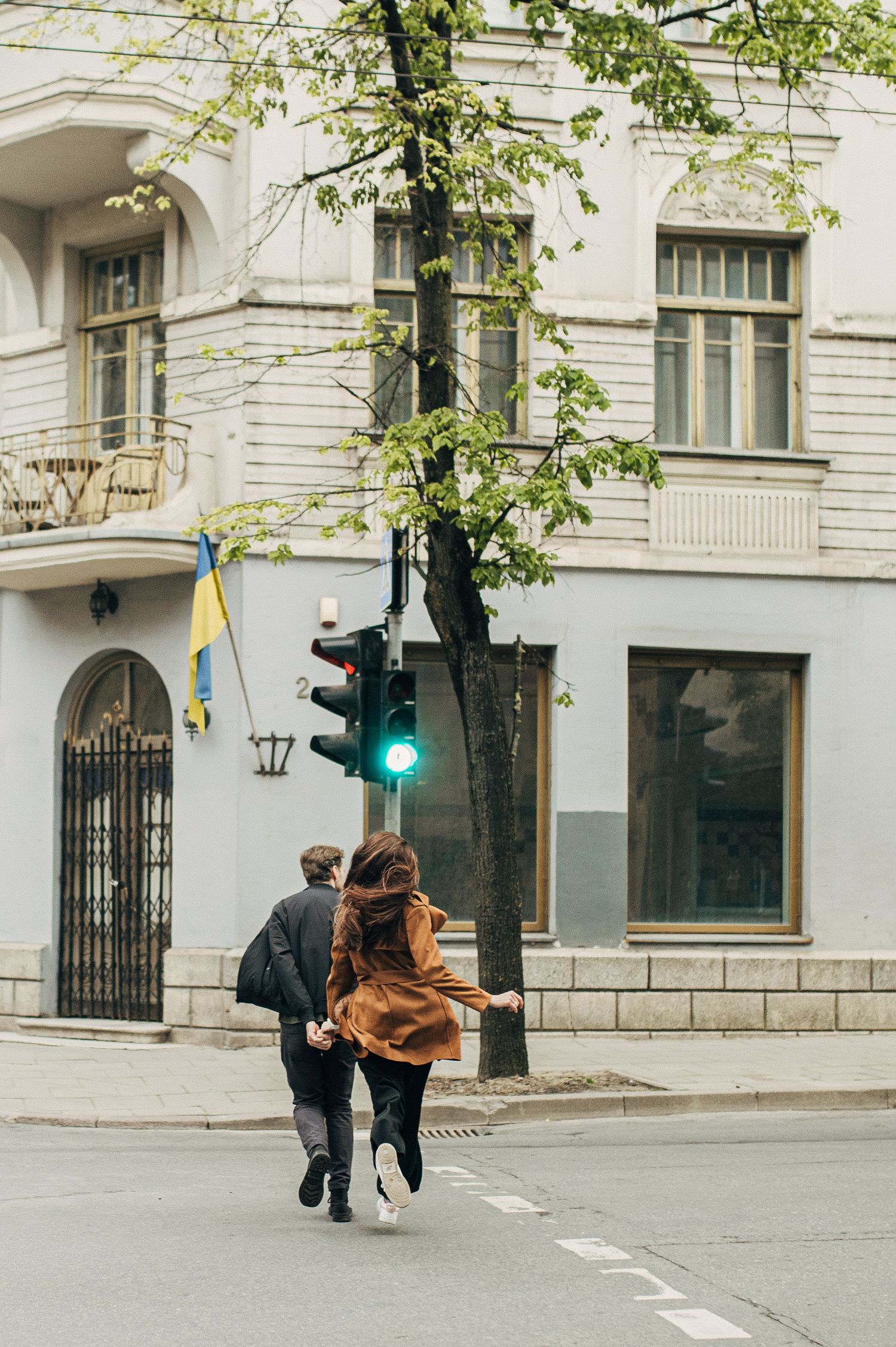 A couple dancing and twirling on a city street with classical architecture in the background.