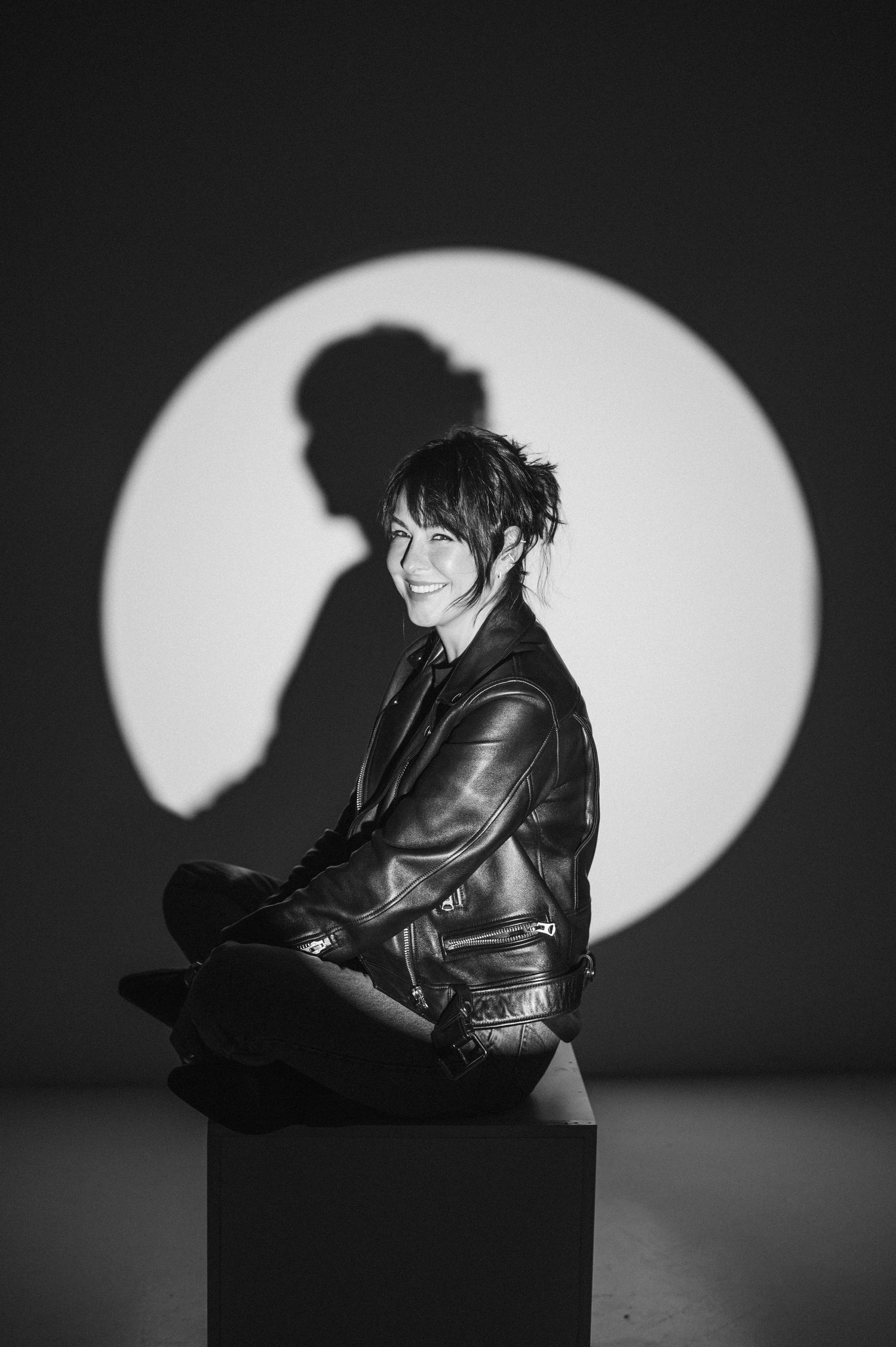 Dramatic black and white portrait with leather jacket against spotlight backdrop.
