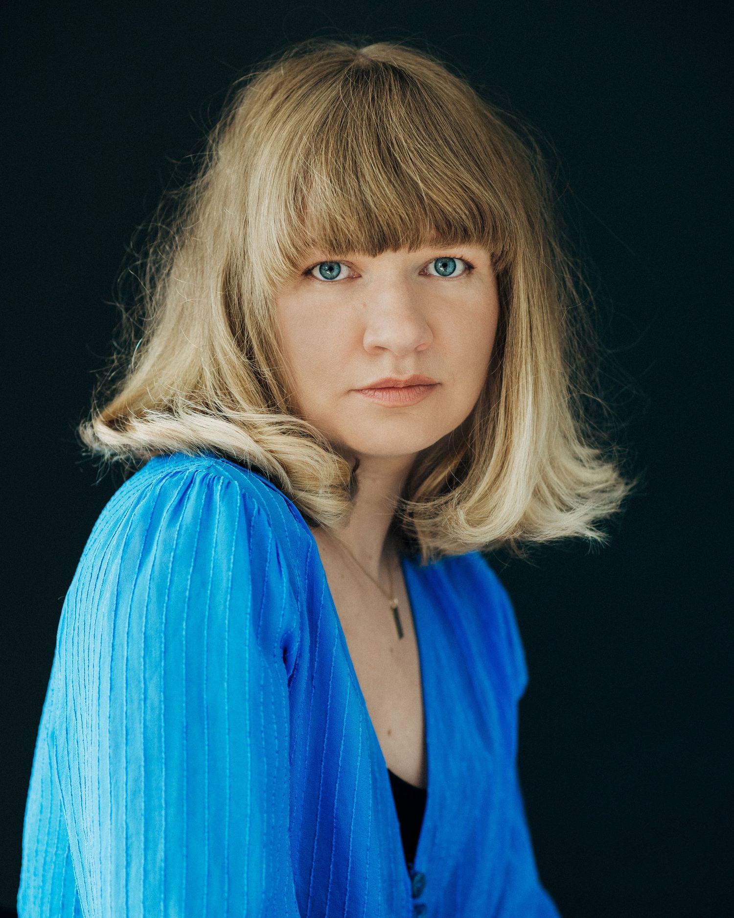 A series of portraits showing a person with blonde hair and bangs wearing a vibrant blue outfit against a dark background.