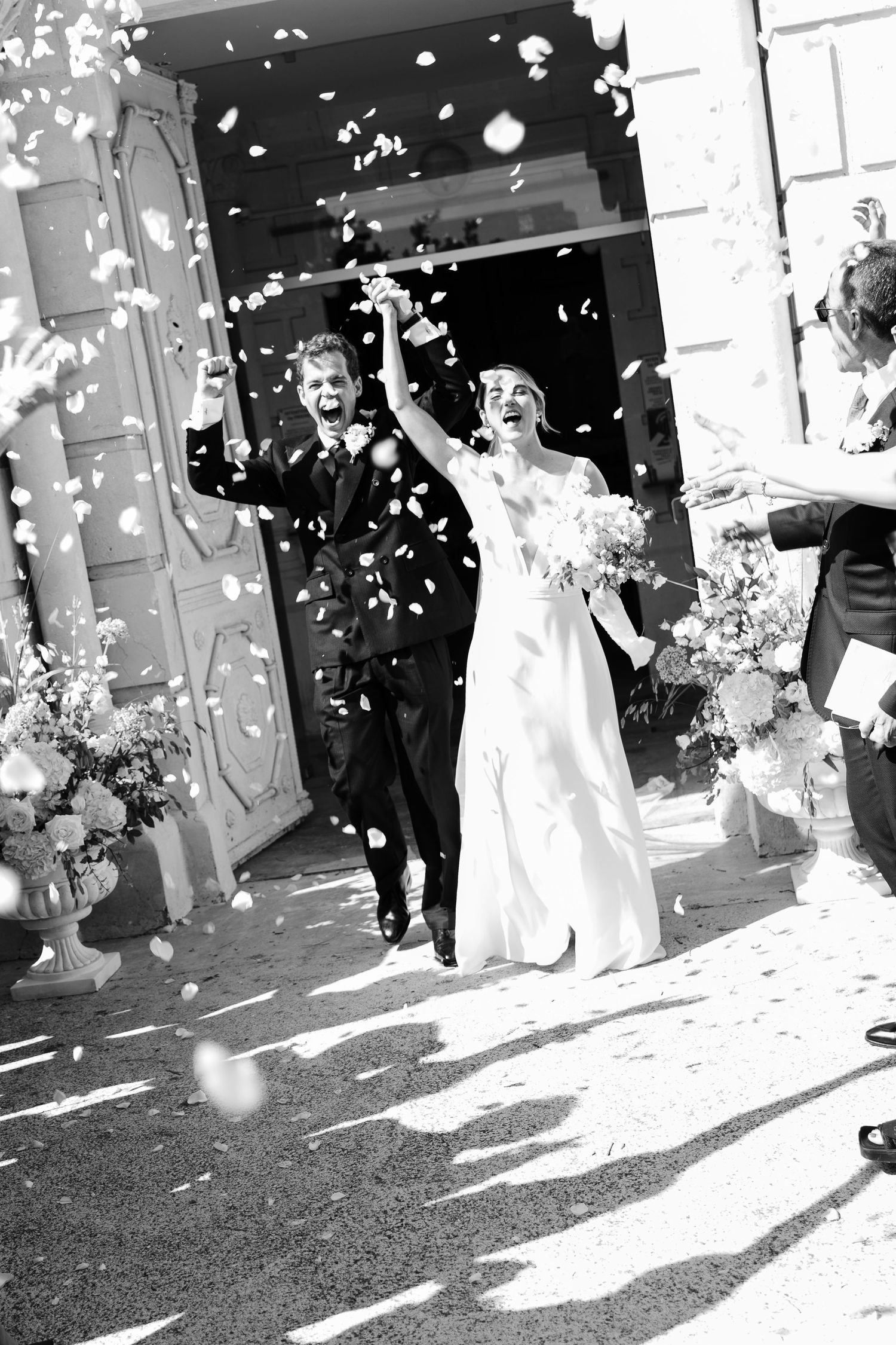 Photo de mariage premium au sanctuaire de Roussas, les mariés en sortie d'église avec les invités qui envoient des pétales de rose.