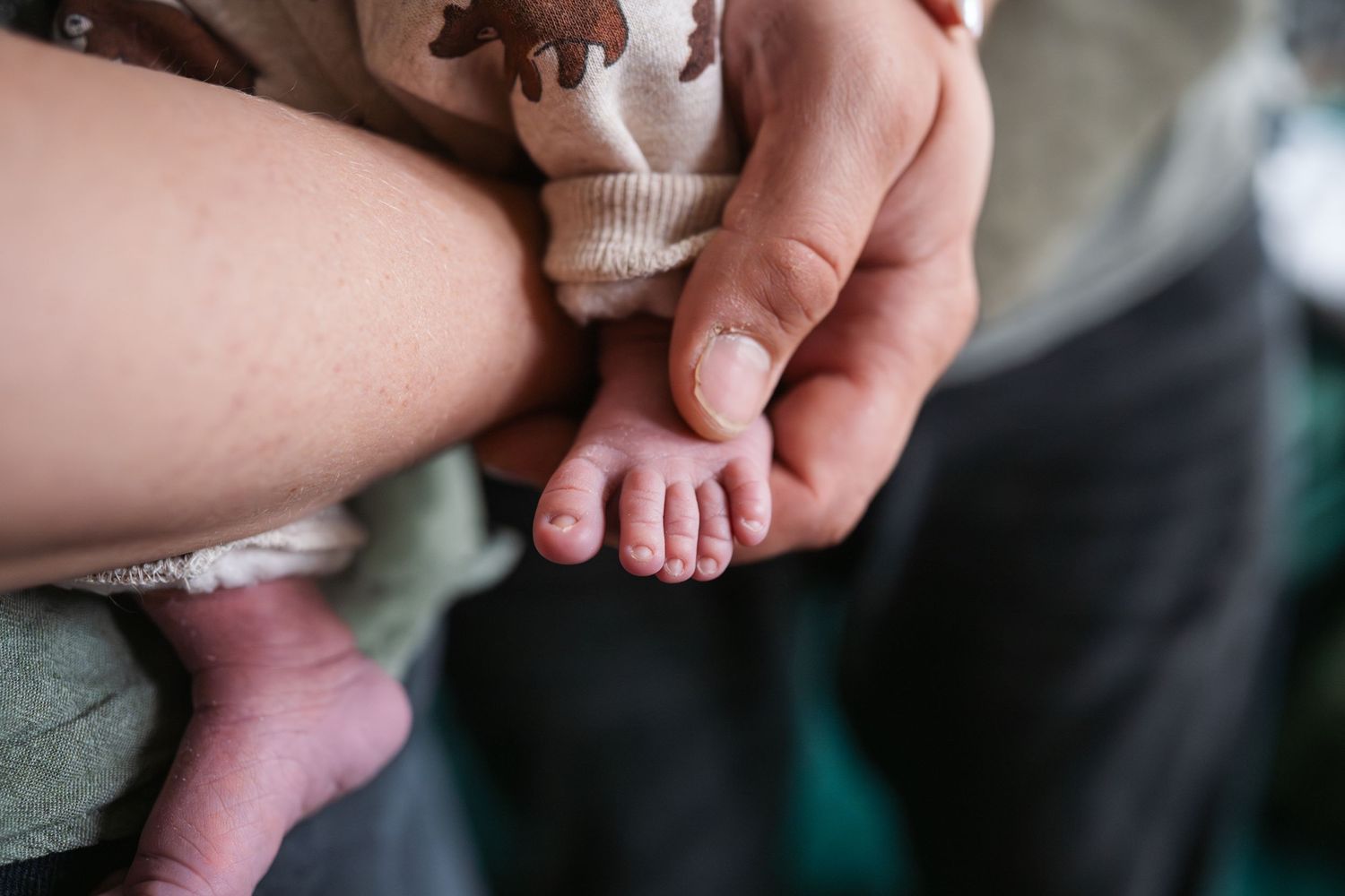Close-up of an adult hand gently holding tiny newborn baby feet, showcasing delicate toes and soft skin.