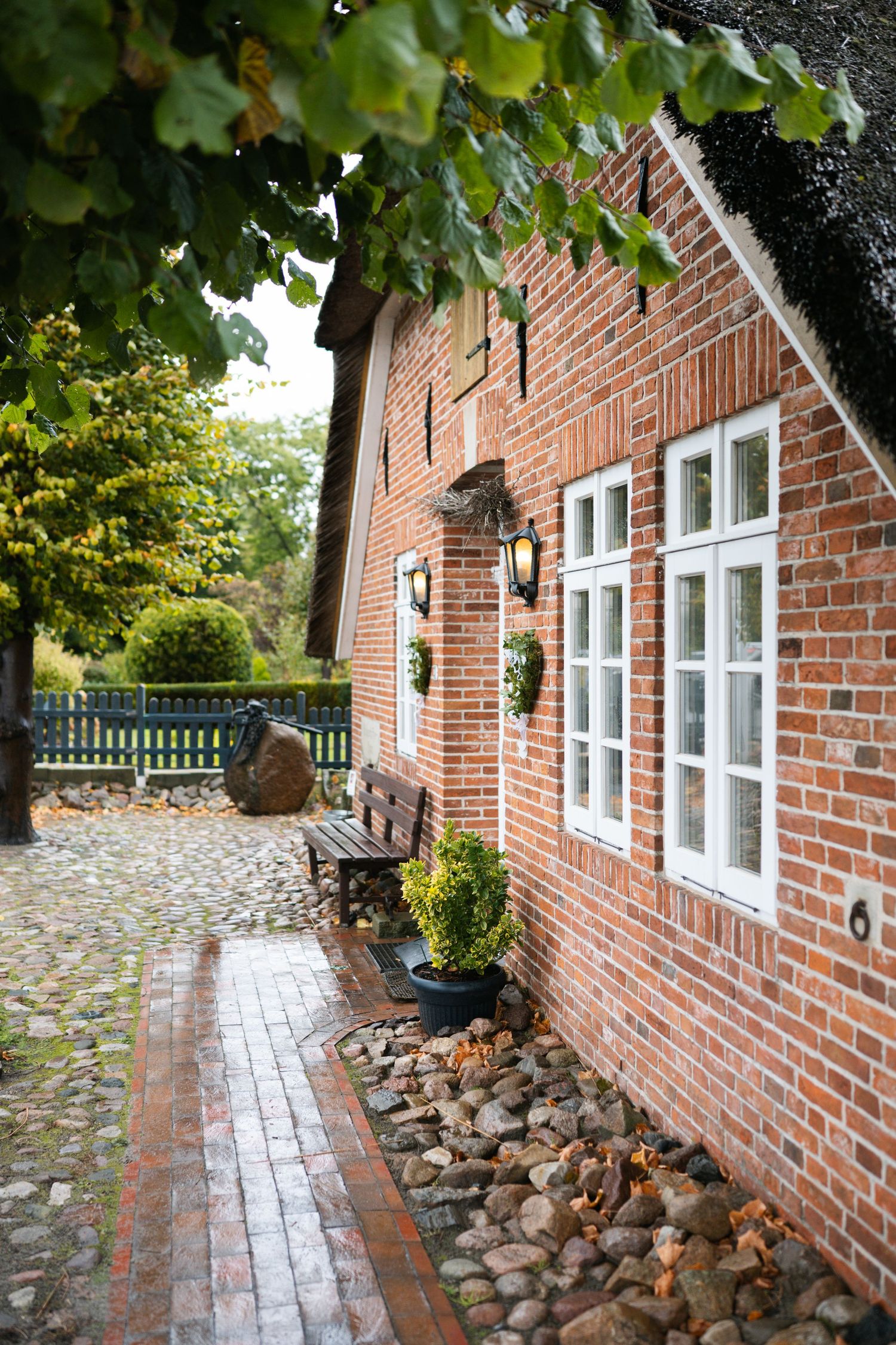 Brick house exterior with stone-lined pathway and green foliage creating a charming garden walkway perspective.