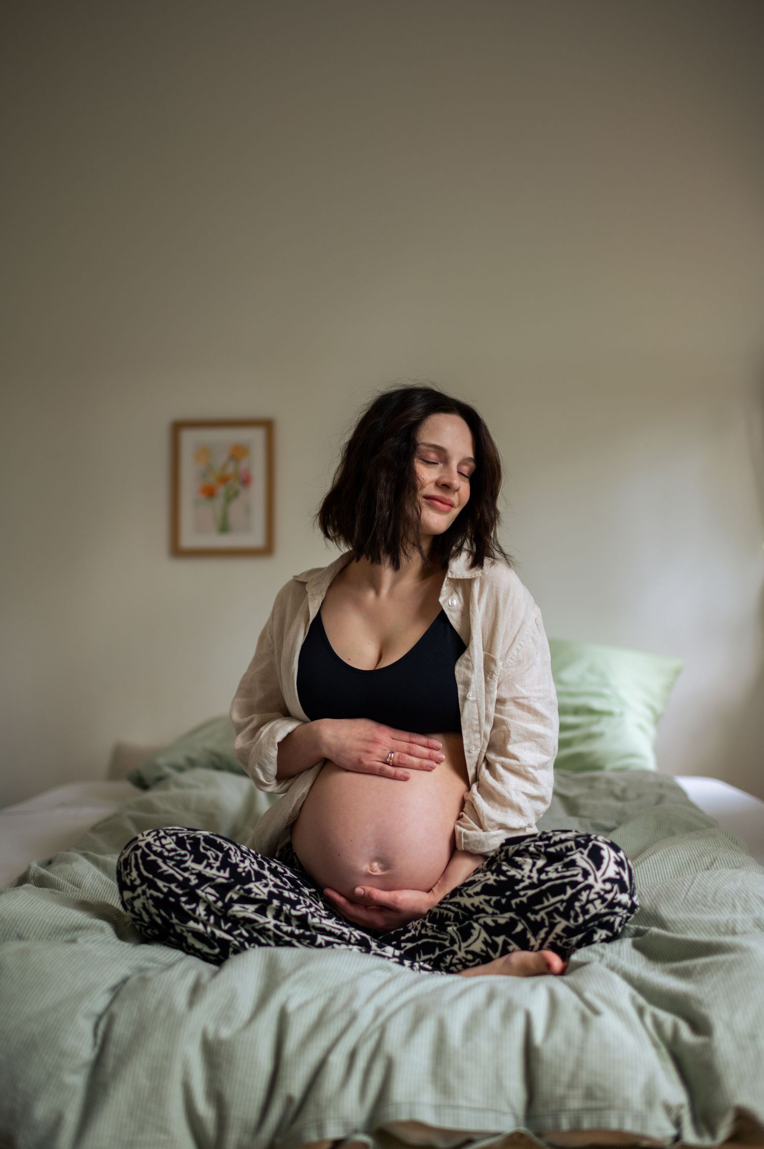 A series of intimate maternity photos showing a pregnant belly in soft lighting on a bed with white linens.