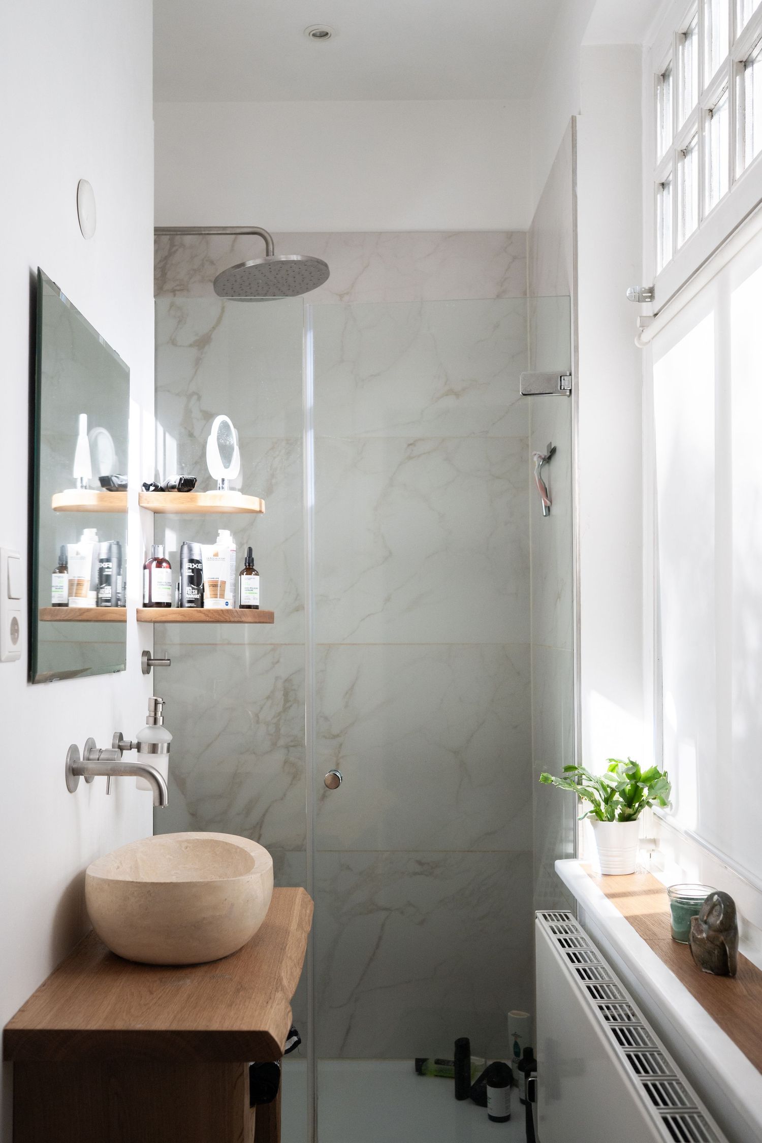 Modern bathroom interior with marble walls, wooden countertops and natural lighting from large windows.