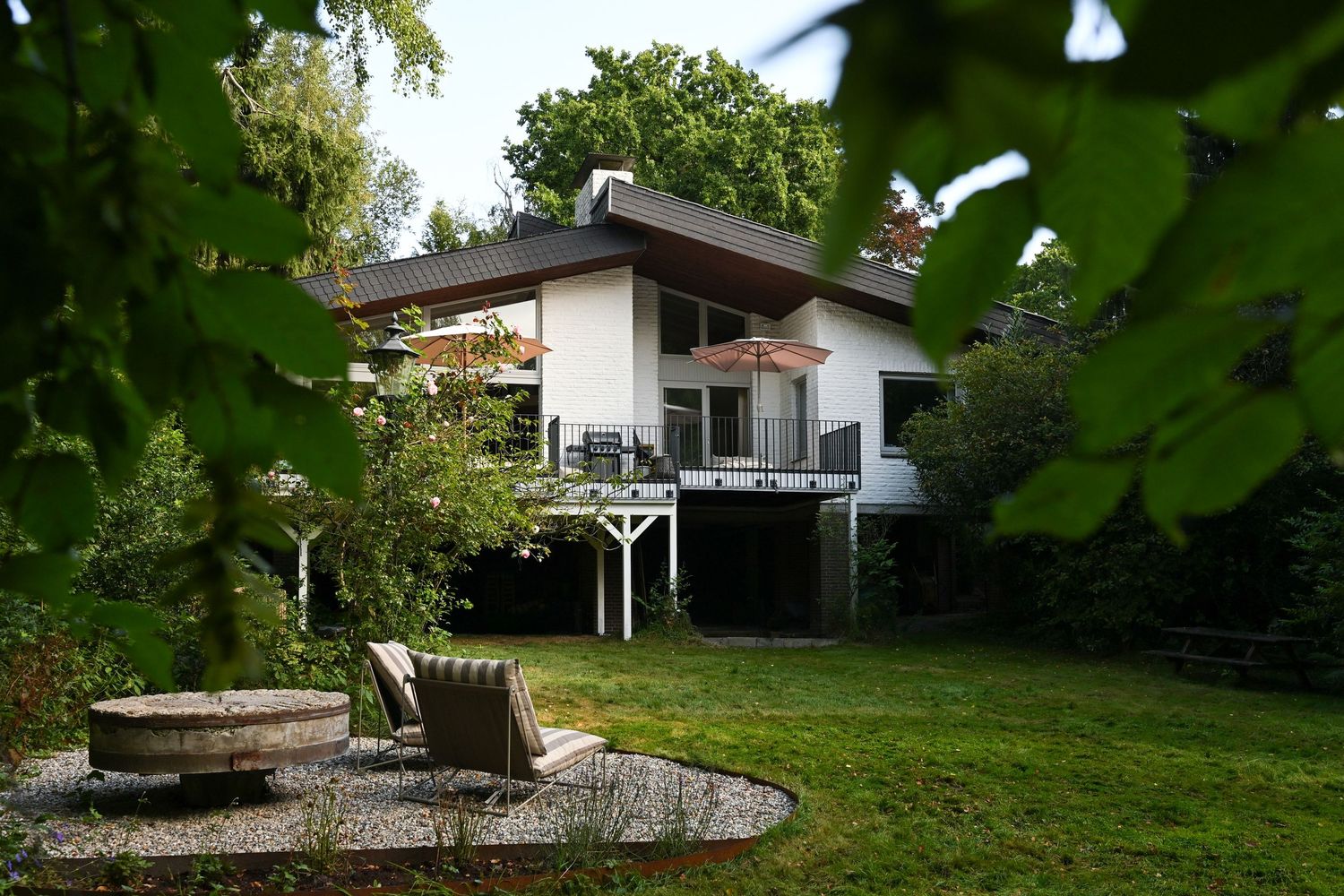 Contemporary white house with deck and garden featuring a curved stone patio area surrounded by lush greenery.