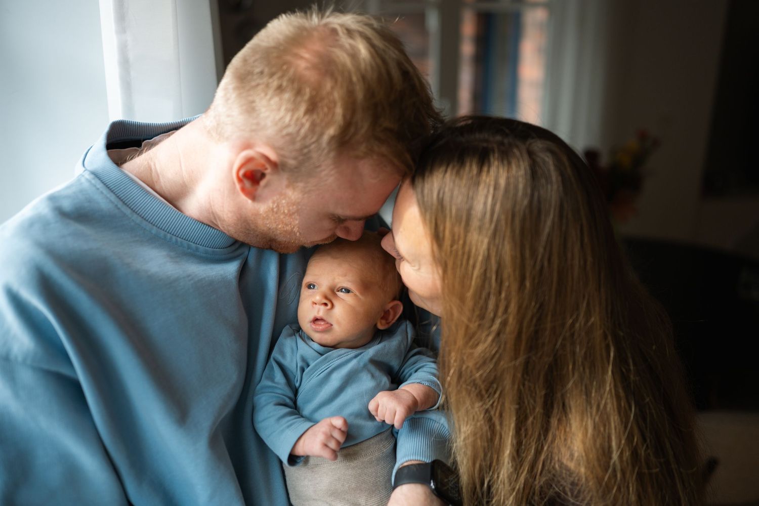 Two parents lovingly hold their newborn baby in blue, sharing a tender family moment together.