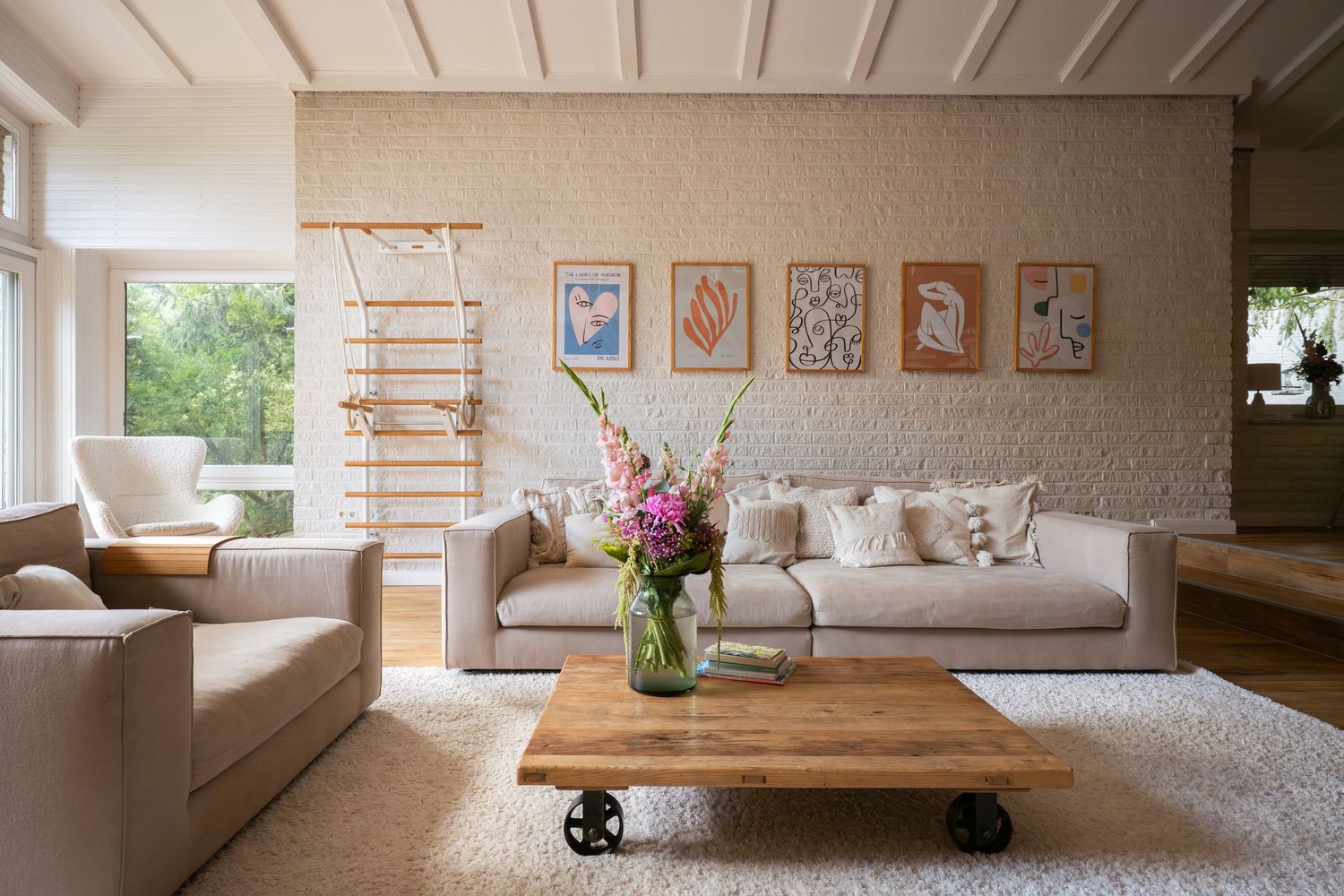 Modern living room with wooden coffee table, beige sofas, wall art gallery and decorative ladder against white brick wall.