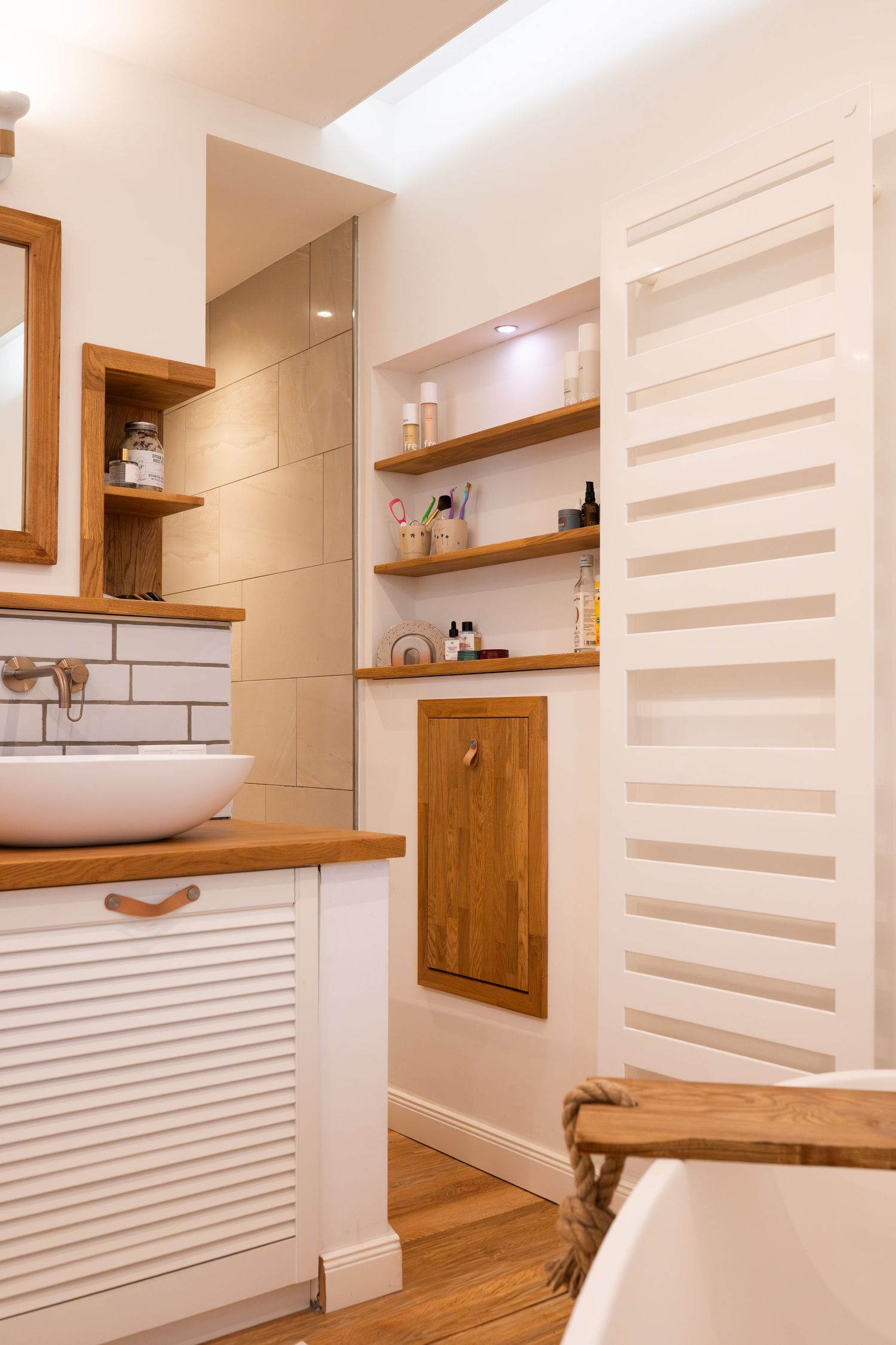 Modern bathroom interior with wooden countertop, vessel sink, and white storage featuring built-in shelving and towel warmer.