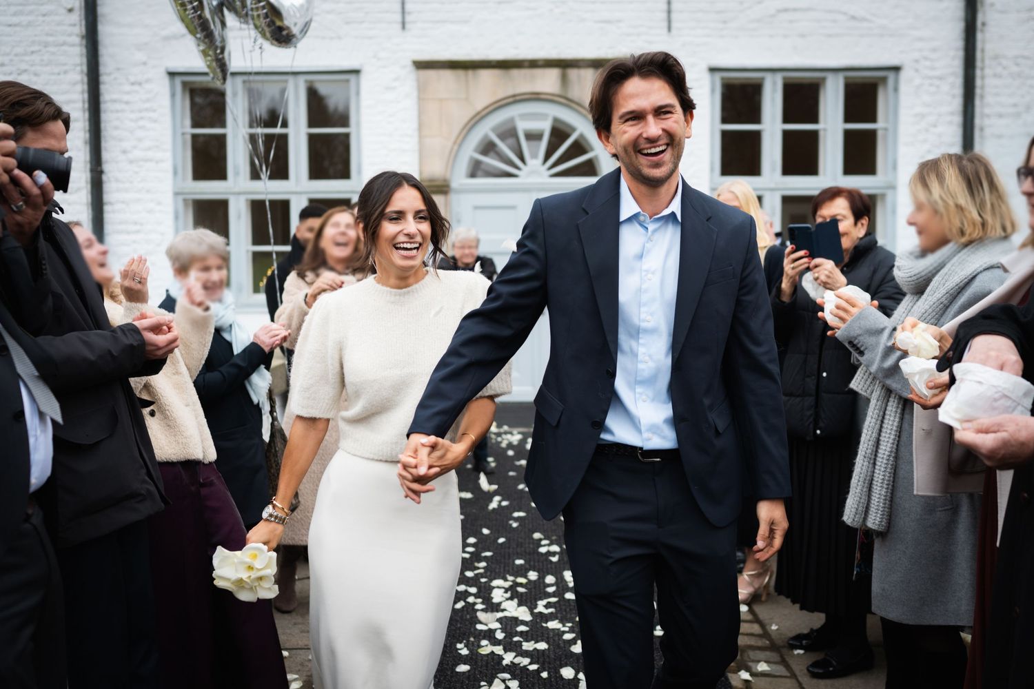 A happy couple walks through confetti after their wedding ceremony while guests celebrate along the path.