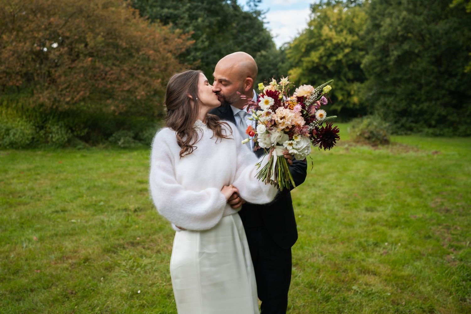 A couple embraces while dancing in a lush green meadow on an autumn day.