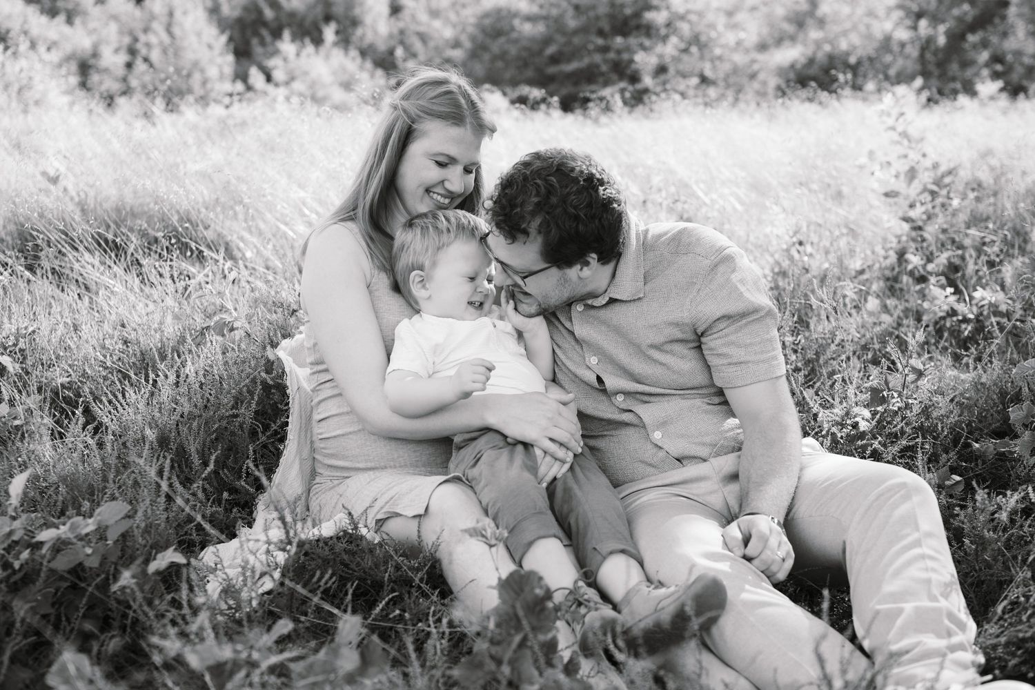 A family sits together in a grassy meadow sharing an intimate black and white moment.