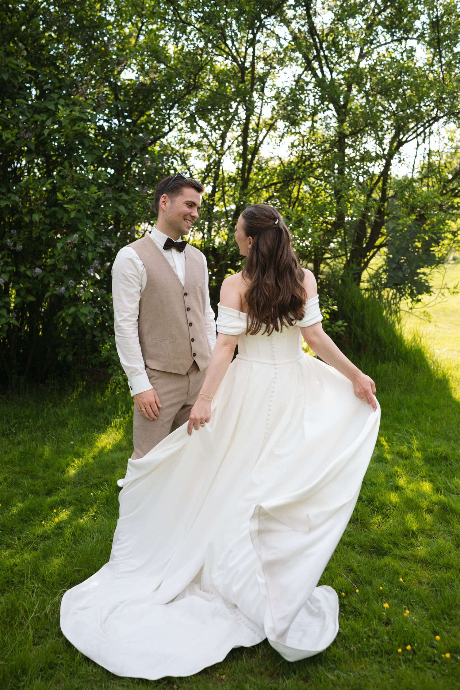 Happy bride and groom walk hand in hand through a lush green garden, bride twirling her white gown.