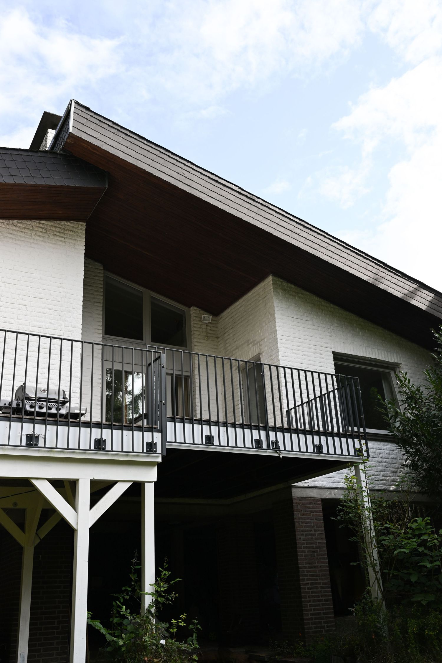 White modern house with dark roof and balcony railing photographed against blue sky.