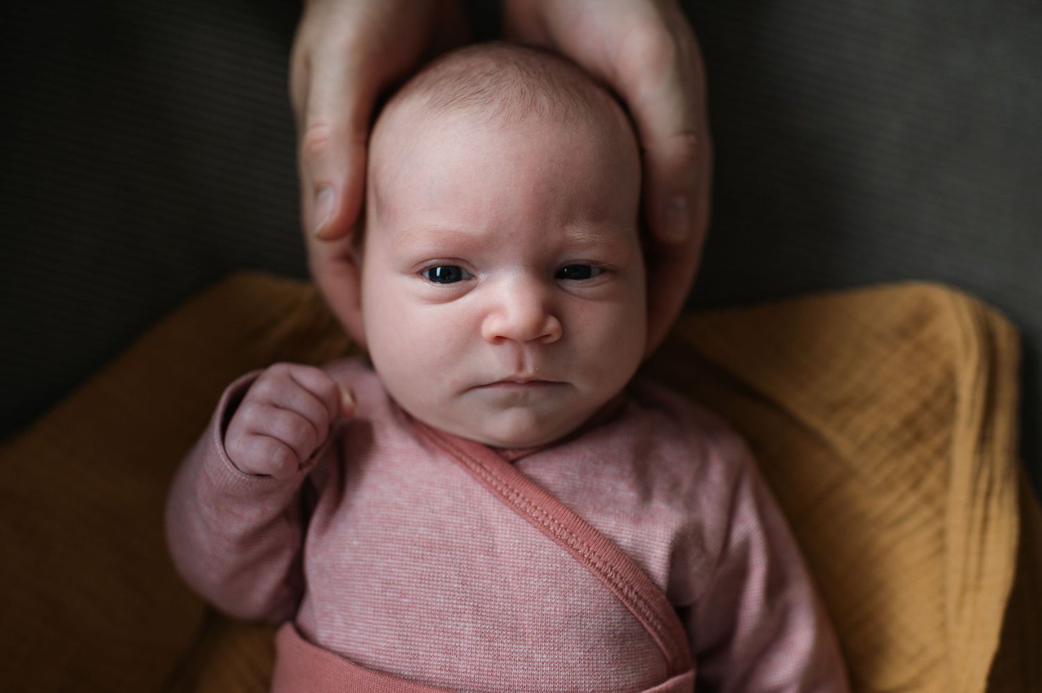 A collage of close-up photos showing a newborn baby wearing pink clothing against dark and yellow backgrounds.
