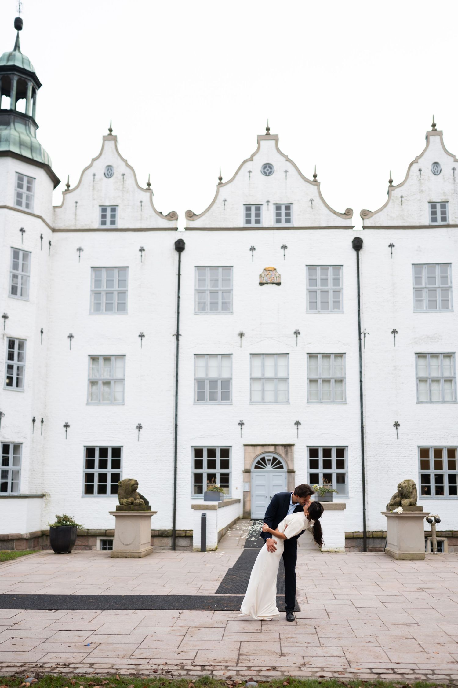 A couple shares a romantic moment in front of white historic buildings with stepped gables and ornate architecture.