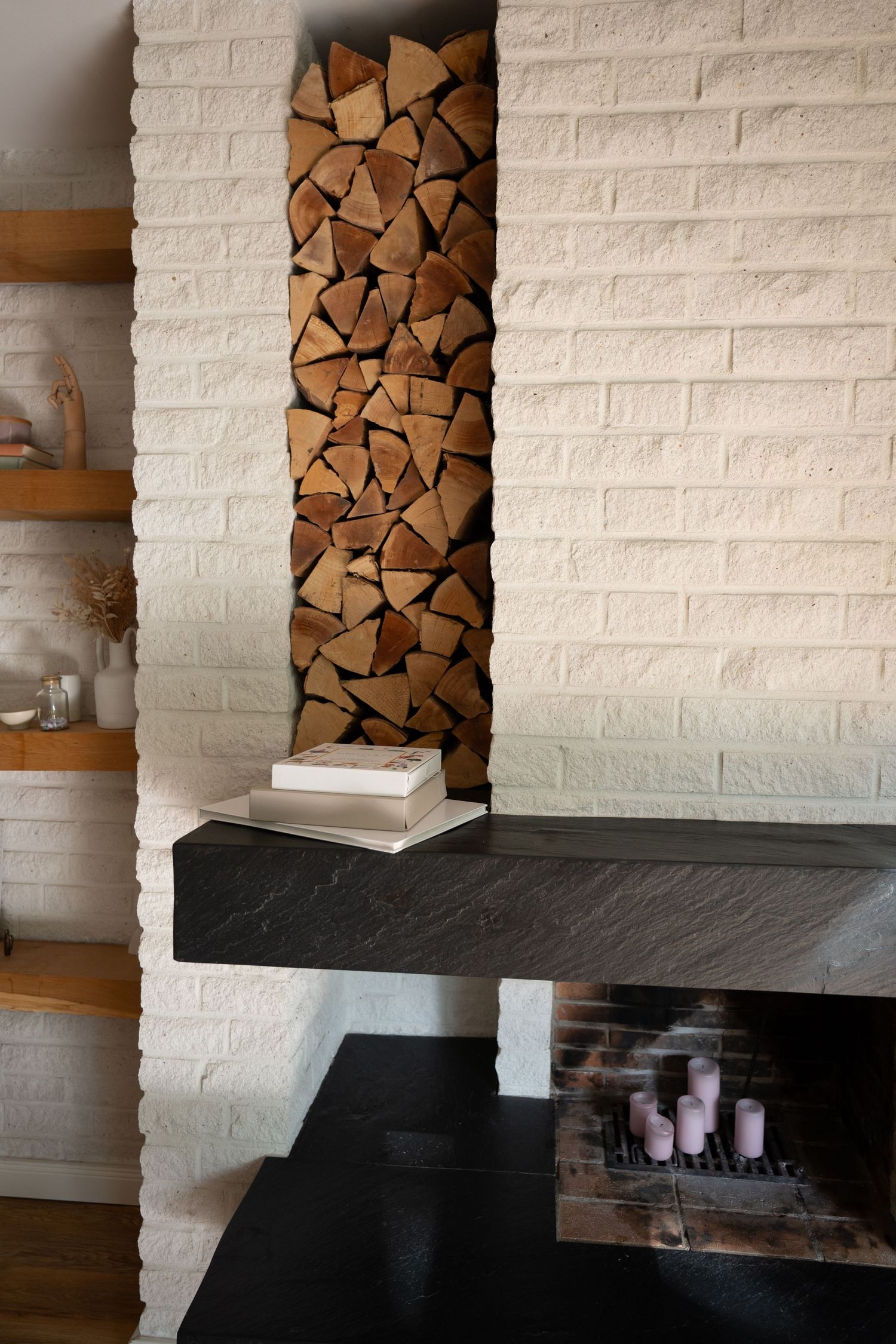 Modern interior design featuring white brick walls with built-in firewood storage and dark floating shelves.