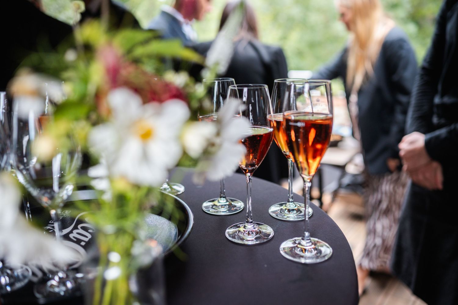 Wine glasses and hands of guests at an outdoor garden party celebration with natural greenery in background.