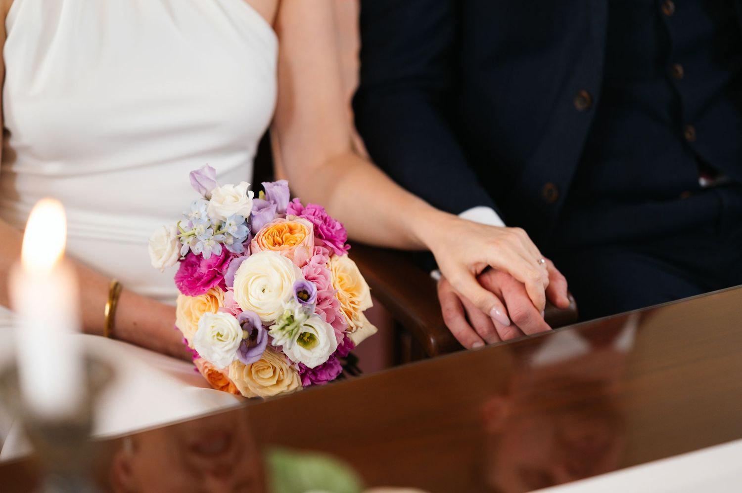 Bride and groom holding hands at wedding ceremony with colorful bridal bouquet of pink, orange, and white flowers.