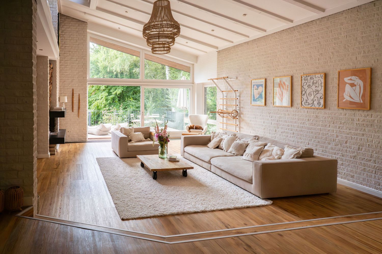 Bright living room with rattan chandelier, beige sectional sofa and framed artwork on white brick wall.