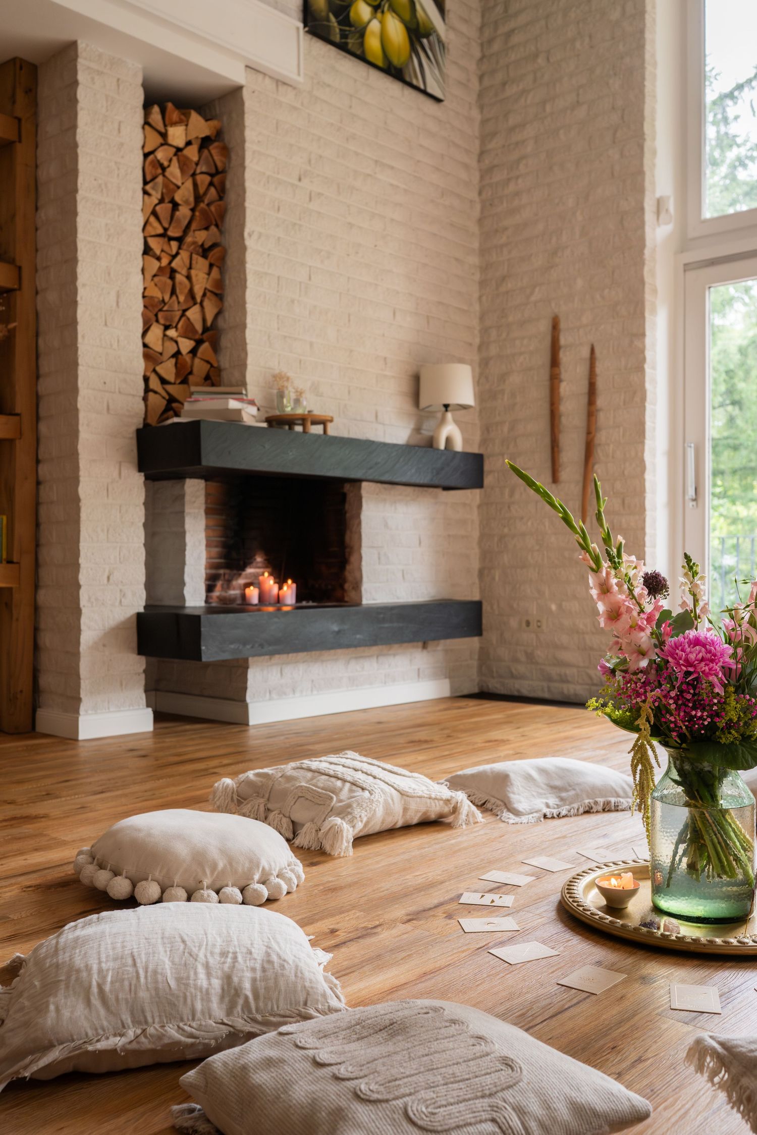 Cozy meditation space with floor cushions, fresh flowers and a fireplace in a bright room with white brick walls.