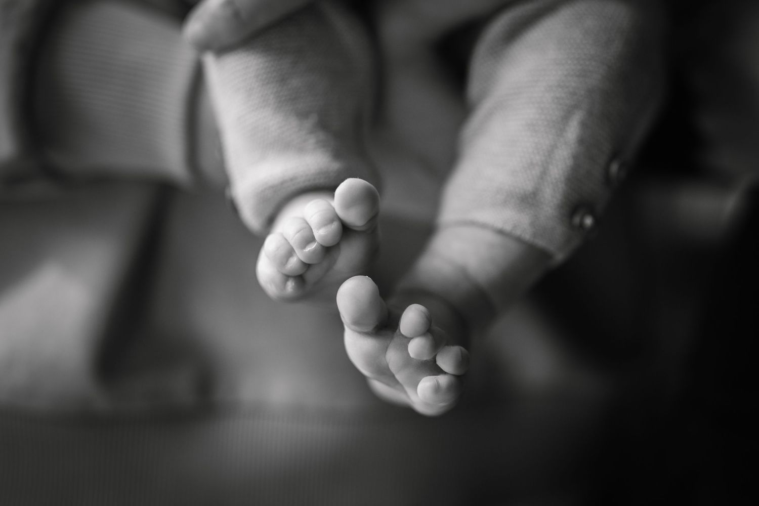 Close-up black and white photo of tiny newborn baby feet and toes, soft focus background.