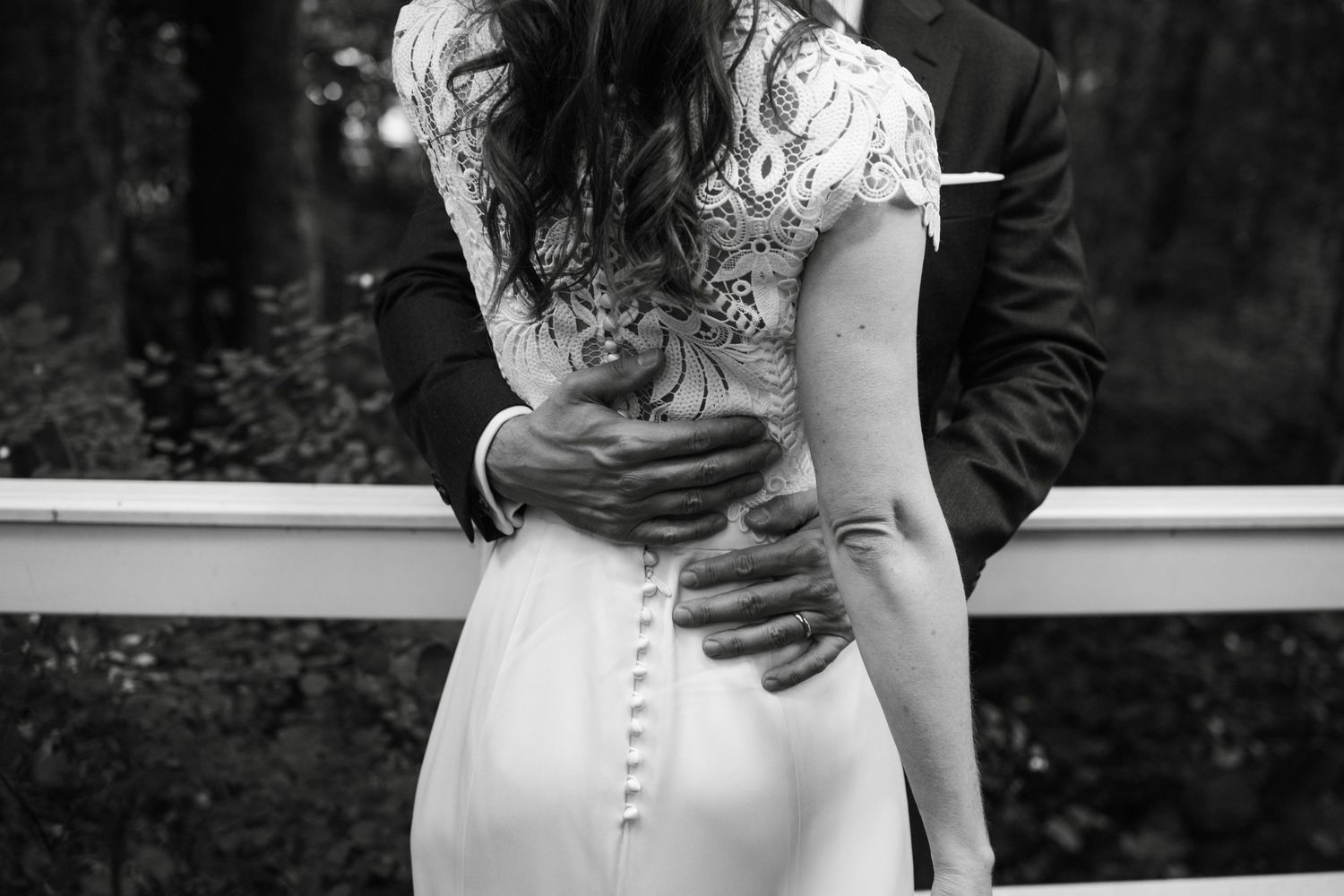 A couple embraces during their wedding ceremony wearing elegant white attire against a dark background.