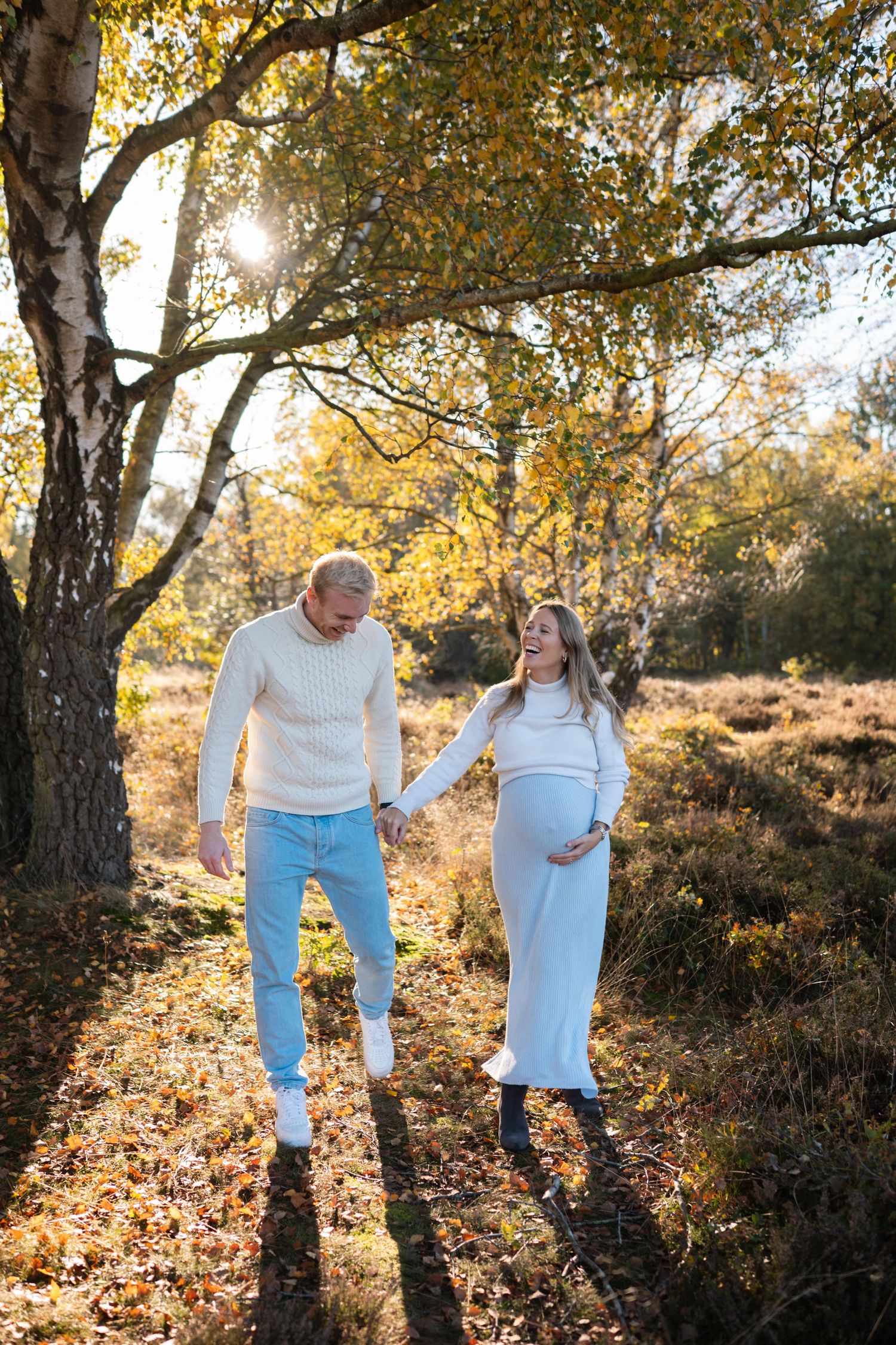 Couple walking together through autumn trees with golden sunlight filtering through branches in a natural setting.