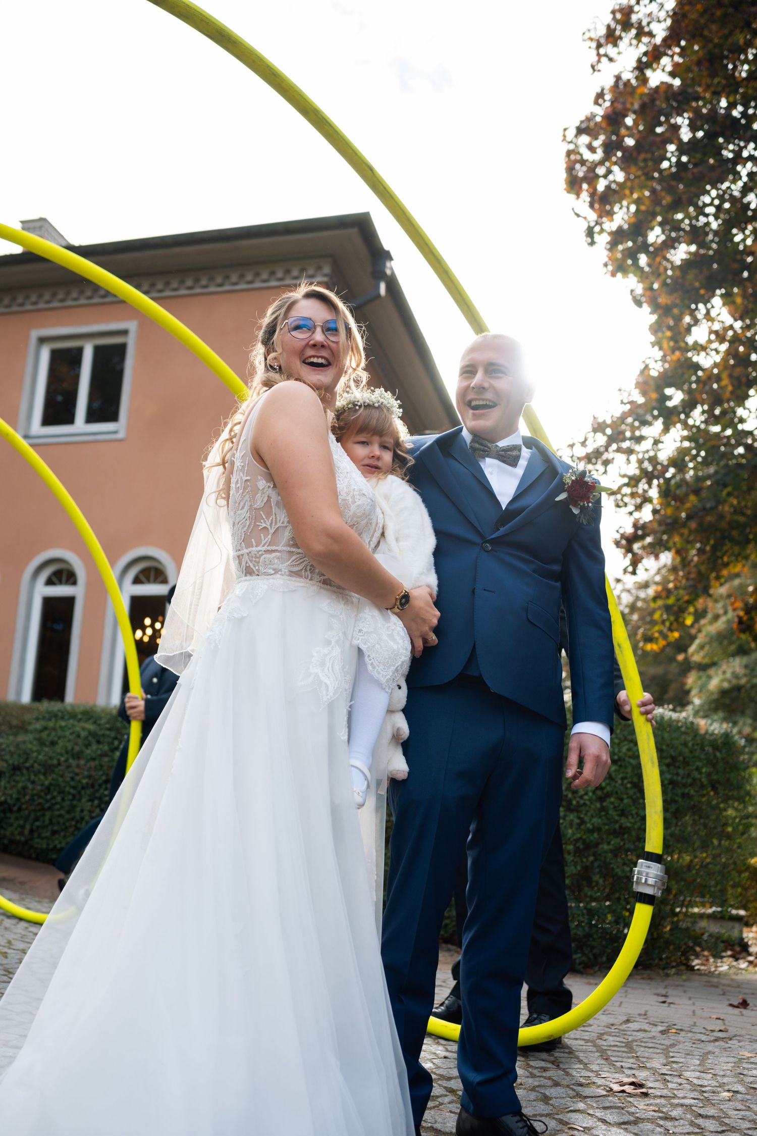 A joyful wedding moment captured outdoors with a unique curved yellow line element framing the scene.