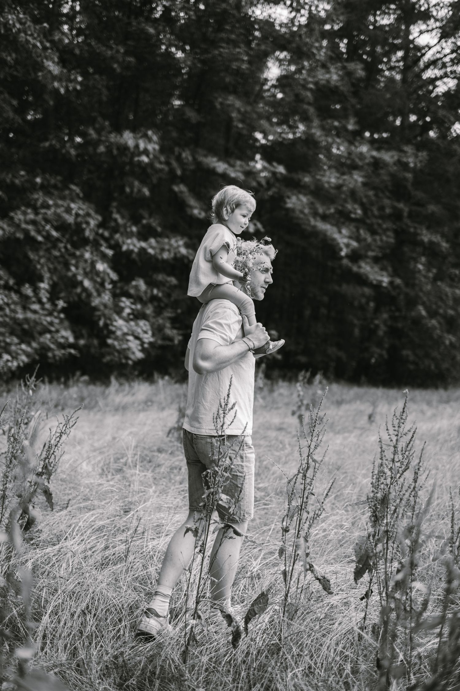 Black and white photo series showing a couple embracing in a tall grass field surrounded by trees.