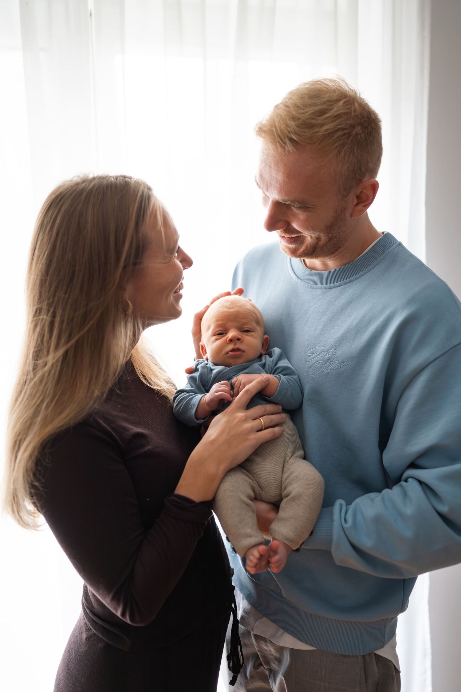 A couple in black and blue sweaters share tender moments with their baby in a series of candid photos.