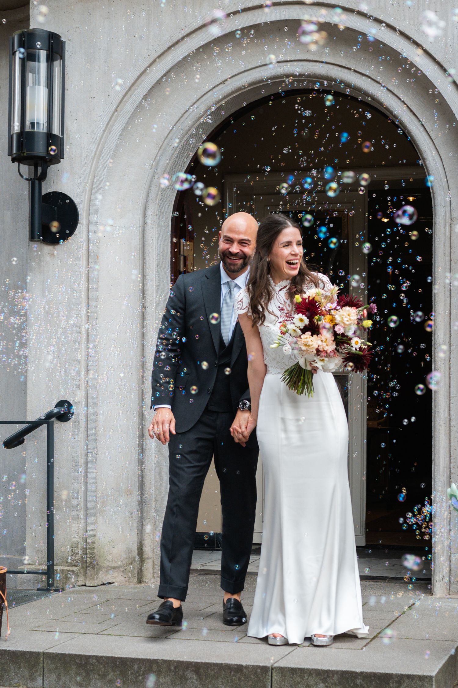 Newlyweds exit church doorway while guests blow bubbles during wedding celebration.