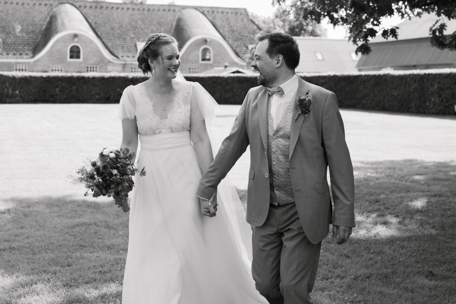 Black and white wedding day moment captured outdoors with couple laughing together in a garden setting.