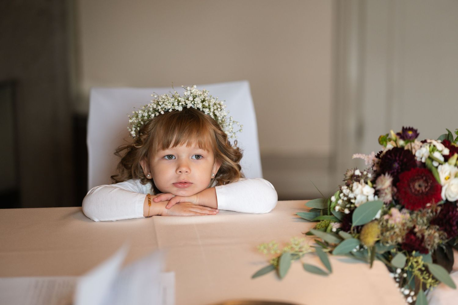 A flower crown adorns a soft pillow in a dreamy wedding day setting with burgundy and white floral arrangements.