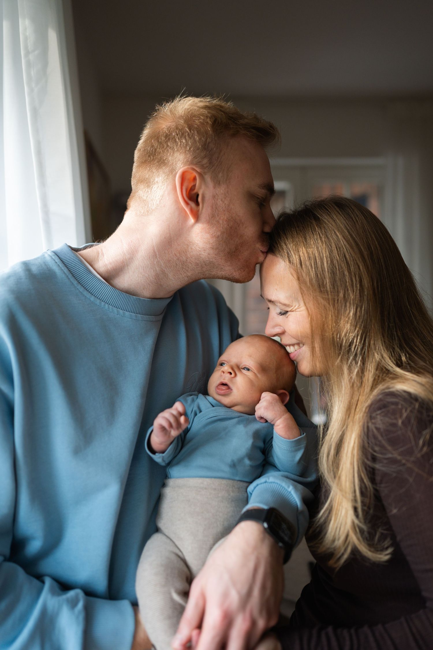 A series of intimate family photos showing tender moments between parents and their baby in matching blue outfits.