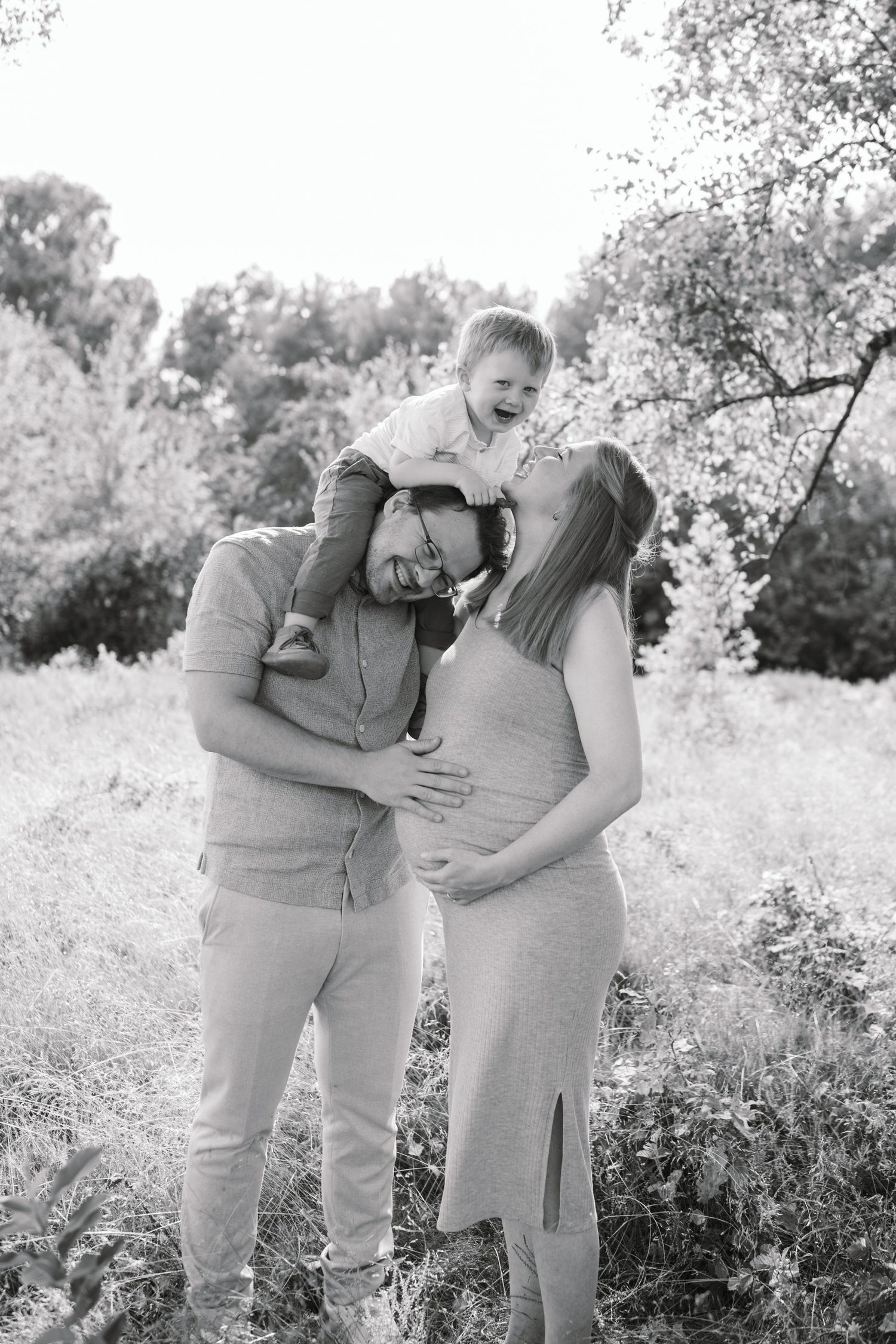 A family shares tender moments together while sitting in a field during a black and white photo session.