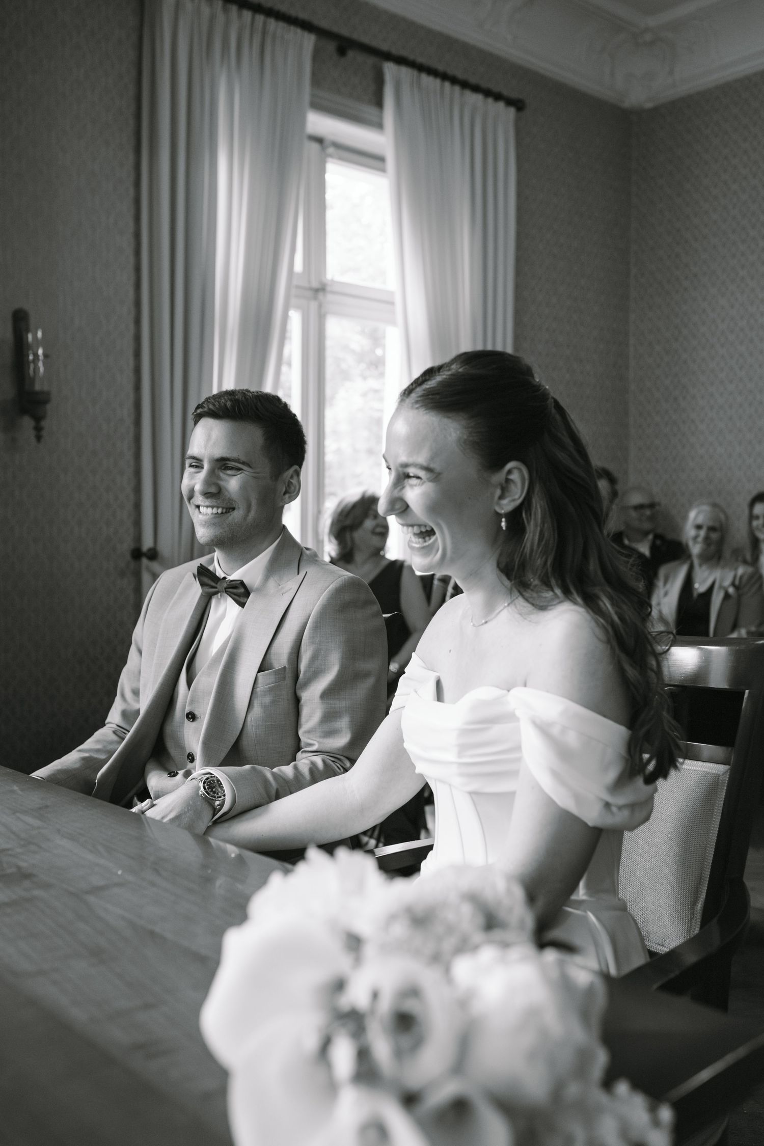 Black and white photo of a smiling bride and groom seated at a table during their wedding ceremony.