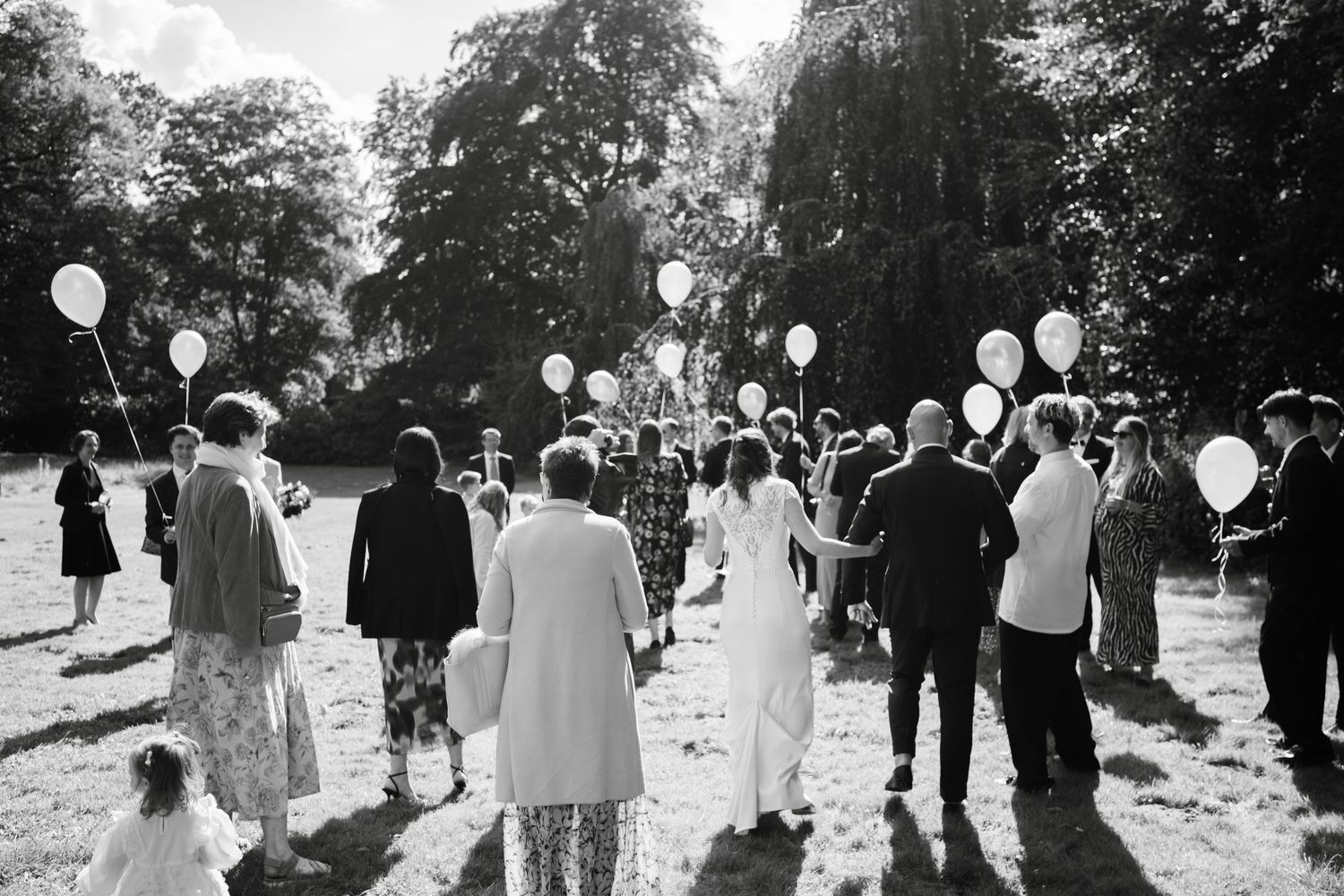 A black and white wedding party releases balloons into the sky during an outdoor celebration.