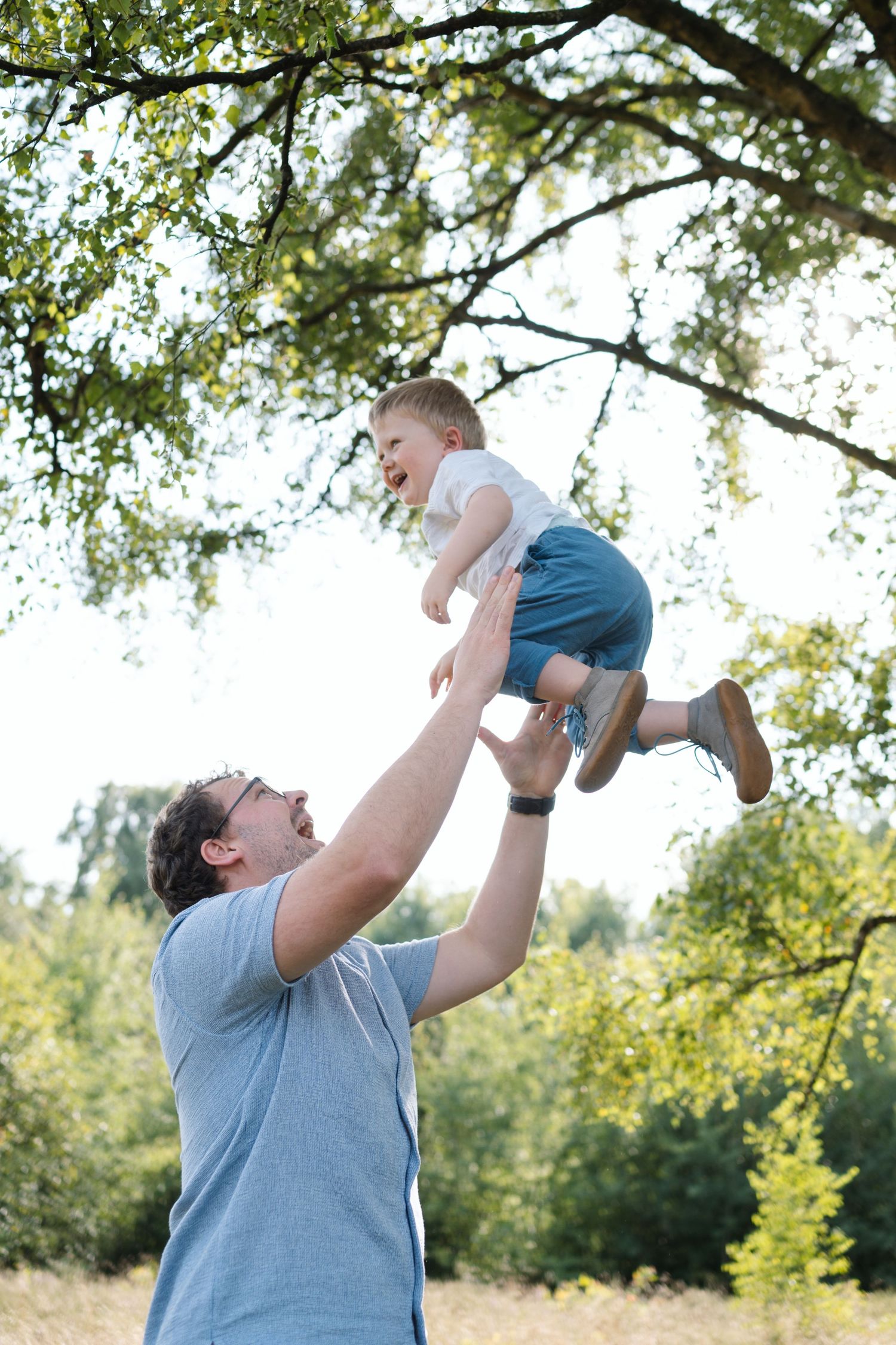 Playful interaction captured in a series of joyful lifts against a backdrop of leafy trees.