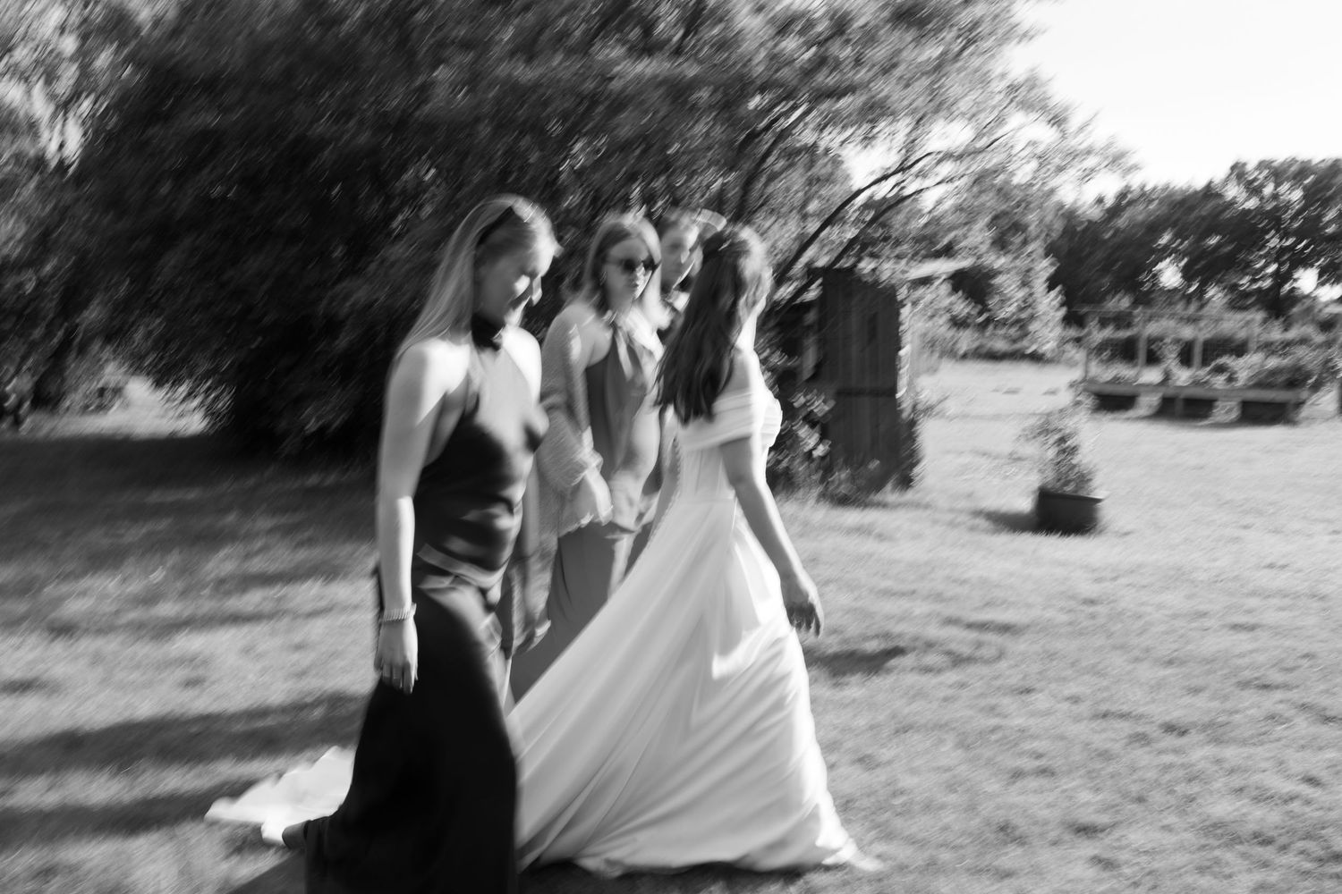 Black and white photo of three women in formal gowns walking outdoors at a wedding celebration.